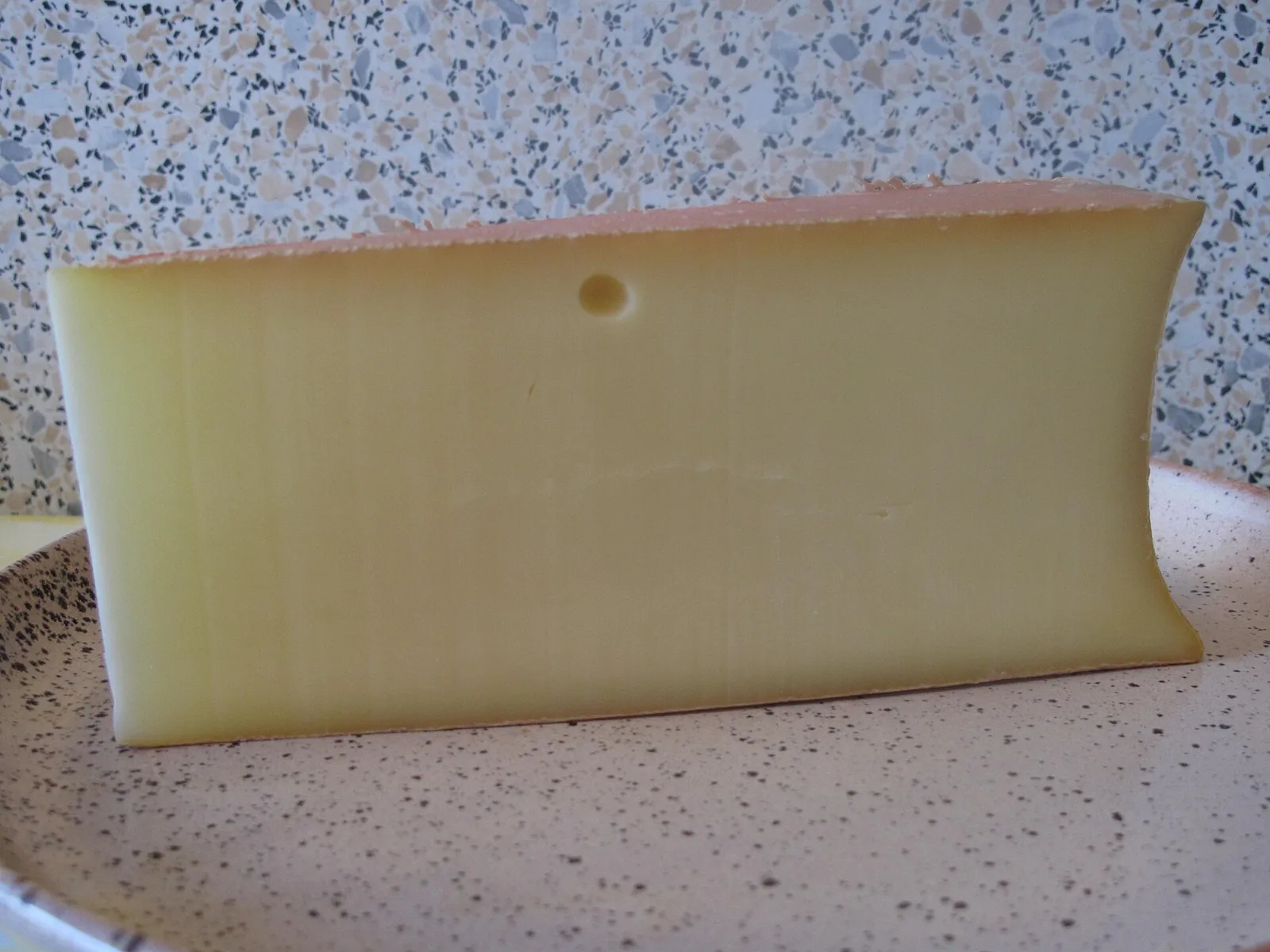 A wedge of Abondance showing its concave side and smooth golden paste