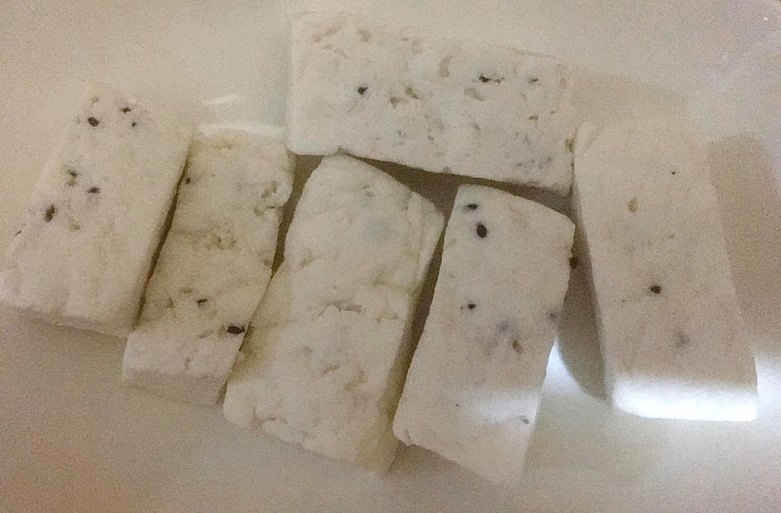 Slices of white akawi cheese speckled with dark seeds laid out on a cream colored plate