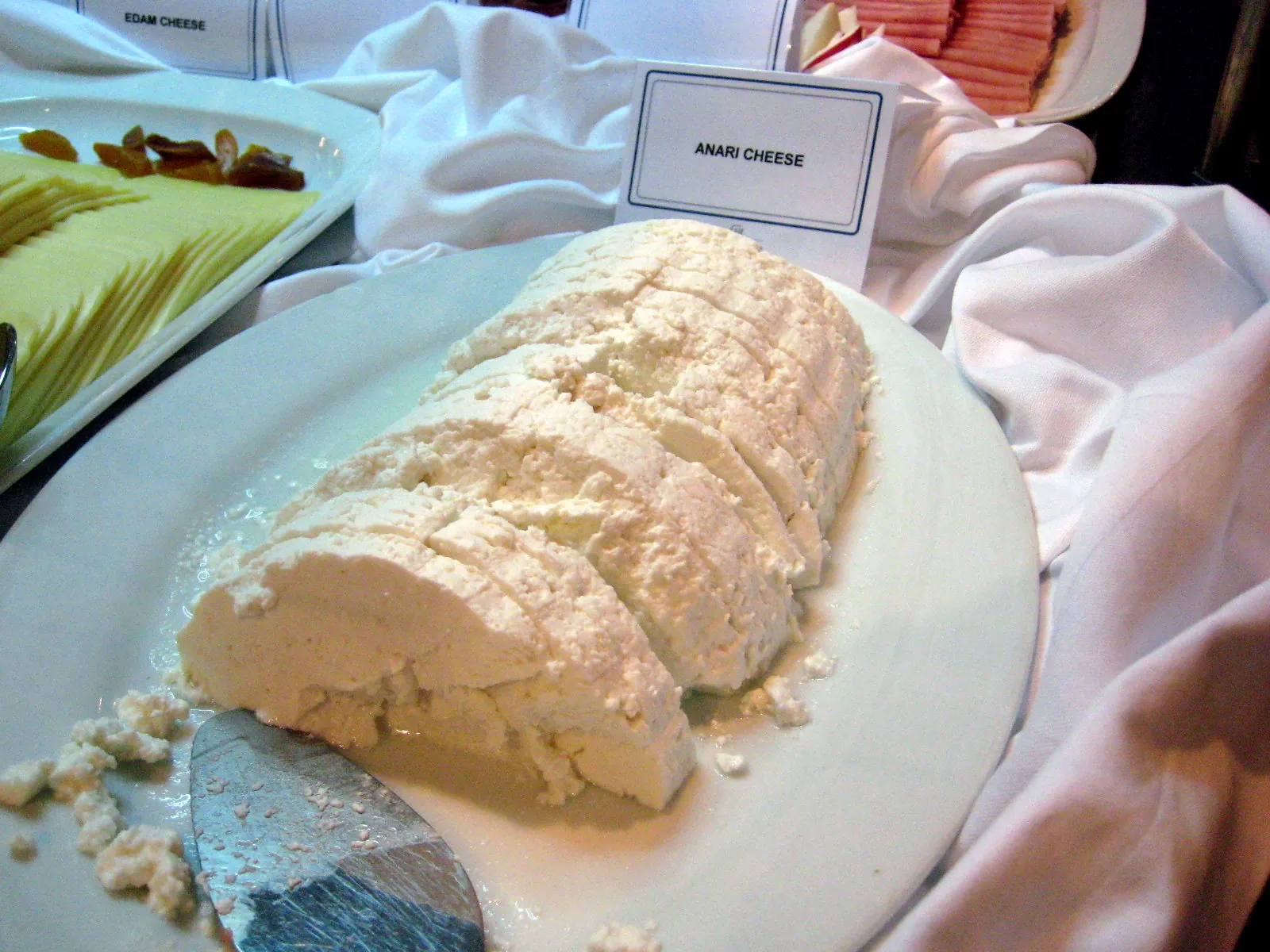 Sliced anari fresh whey cheese heaped on a white plate with a cheese knife at a hotel breakfast buffet