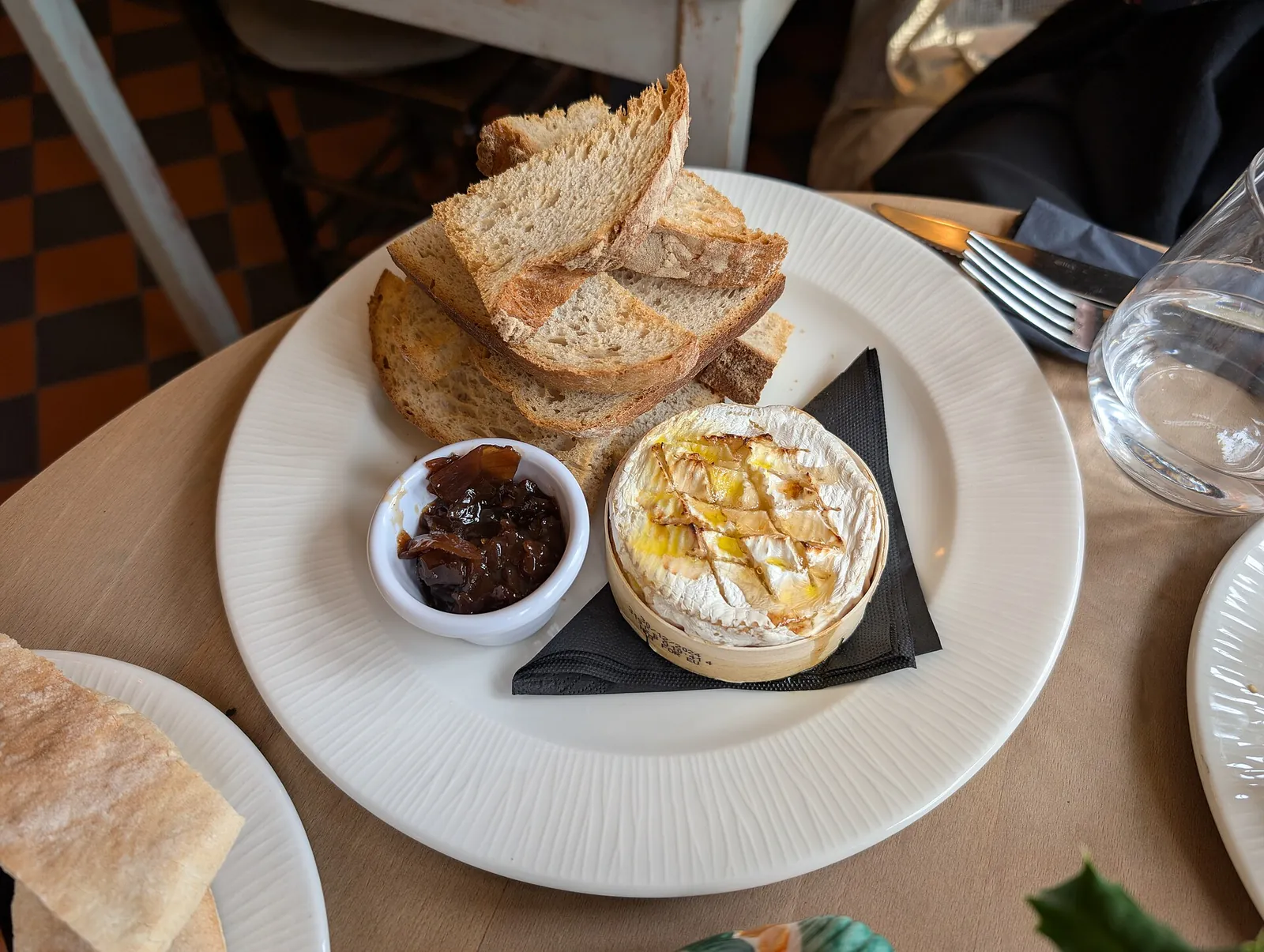 A small round of baked Camembert in its wooden box with a golden, bubbling top, served with sliced bread and a dish of chutney.