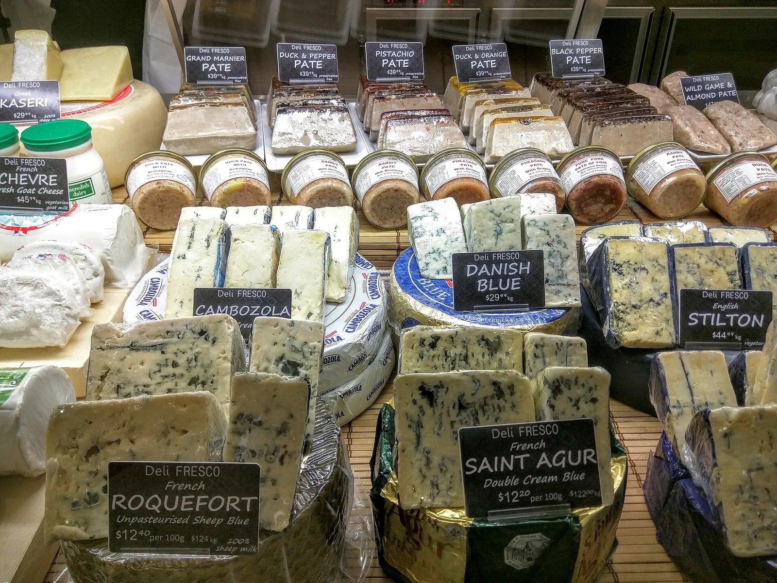 A deli case of blue cheeses labeled Roquefort, Saint Agur, Danish Blue and Stilton