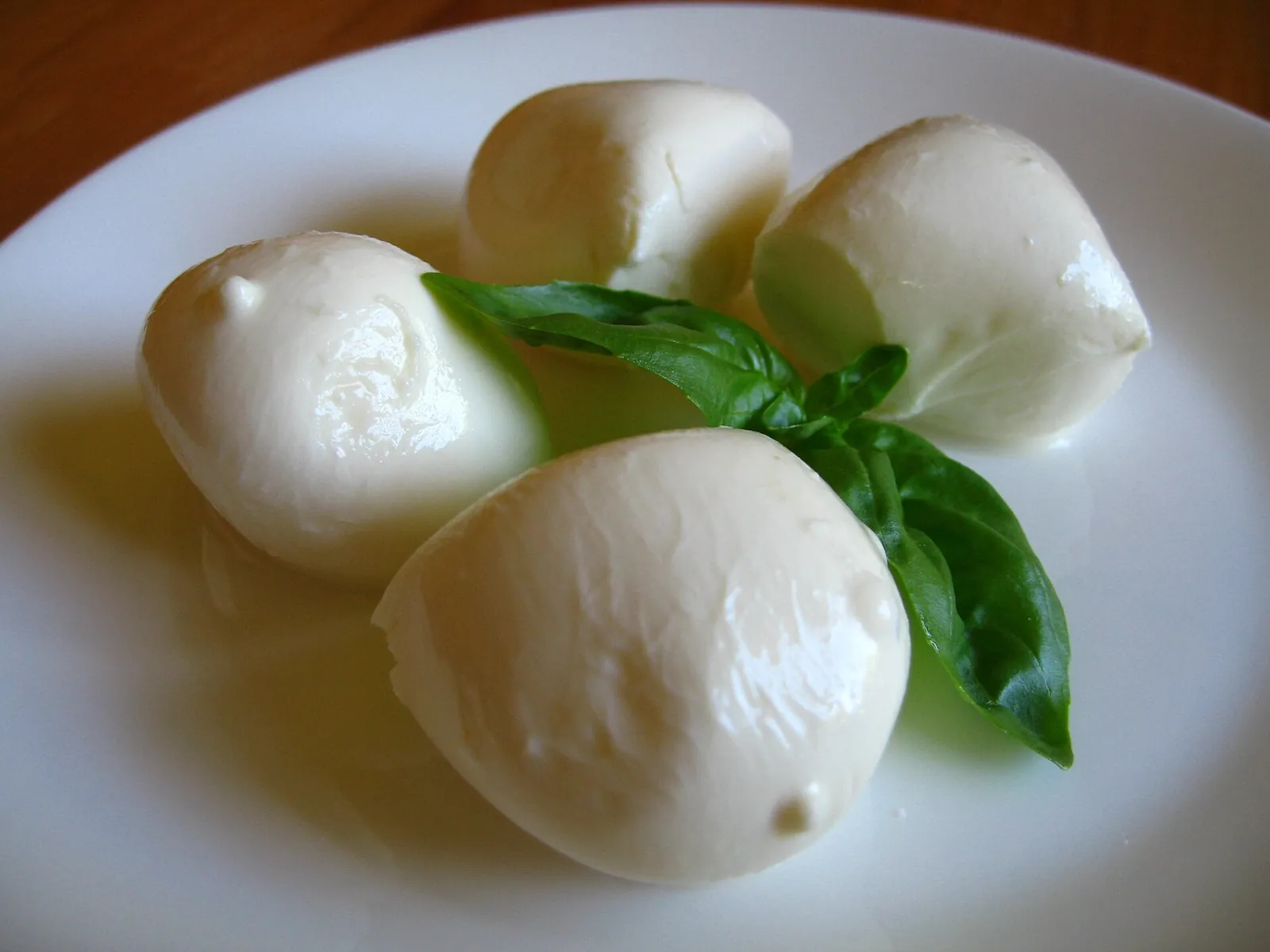 Small balls of fresh mozzarella with a sprig of basil on a white plate