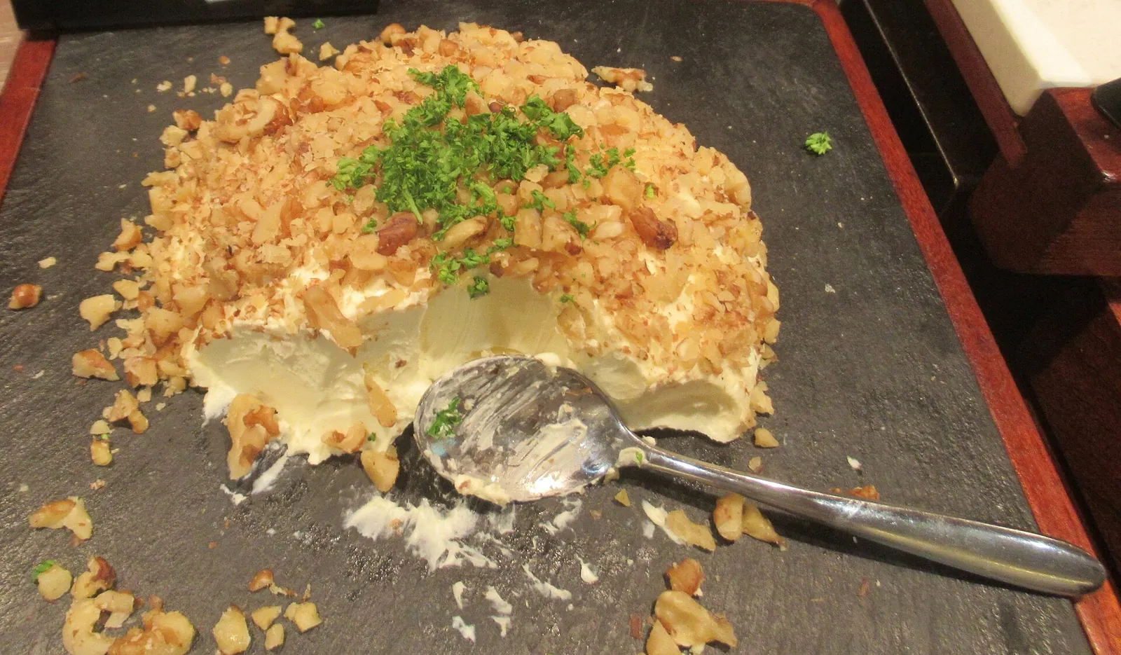 Boursin topped with crumbled walnuts and chives on a slate, with a serving spoon