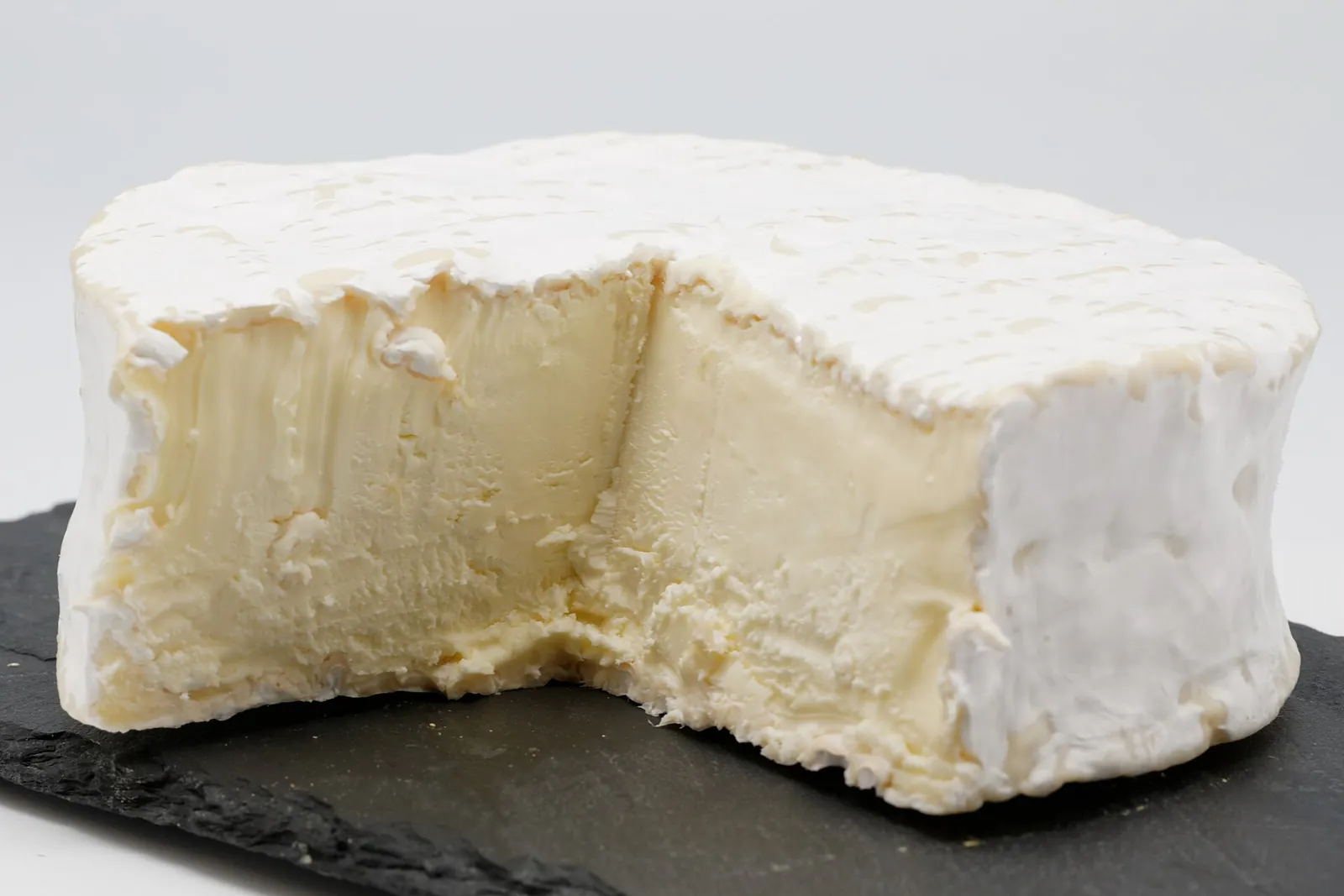 A white bloomy rind Brillat-Savarin round with a wedge cut out showing the pale creamy interior on a slate board