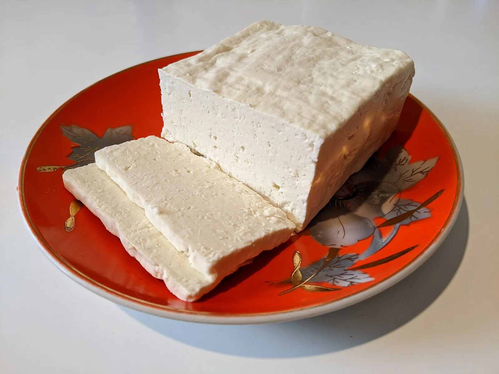 A block of white bryndza sheep cheese cut into slices on a red patterned plate