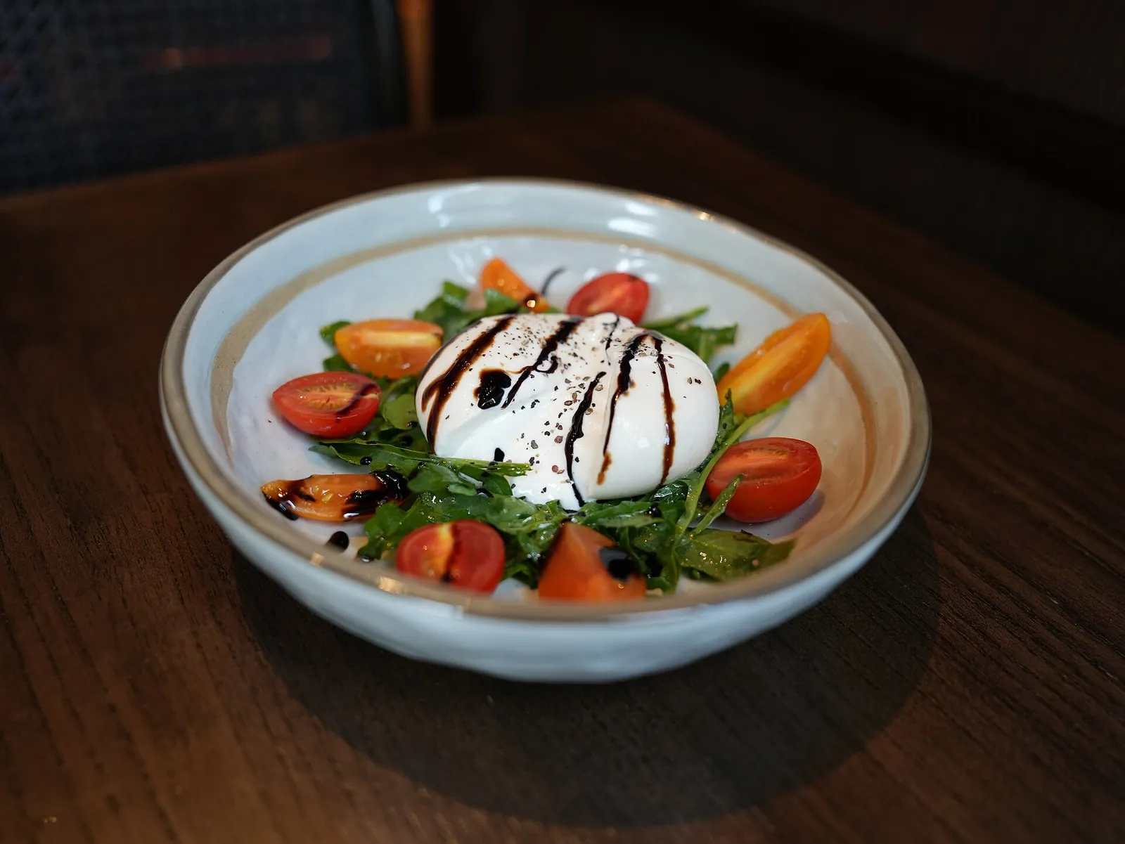 A burrata on cherry tomatoes and arugula, drizzled with balsamic glaze