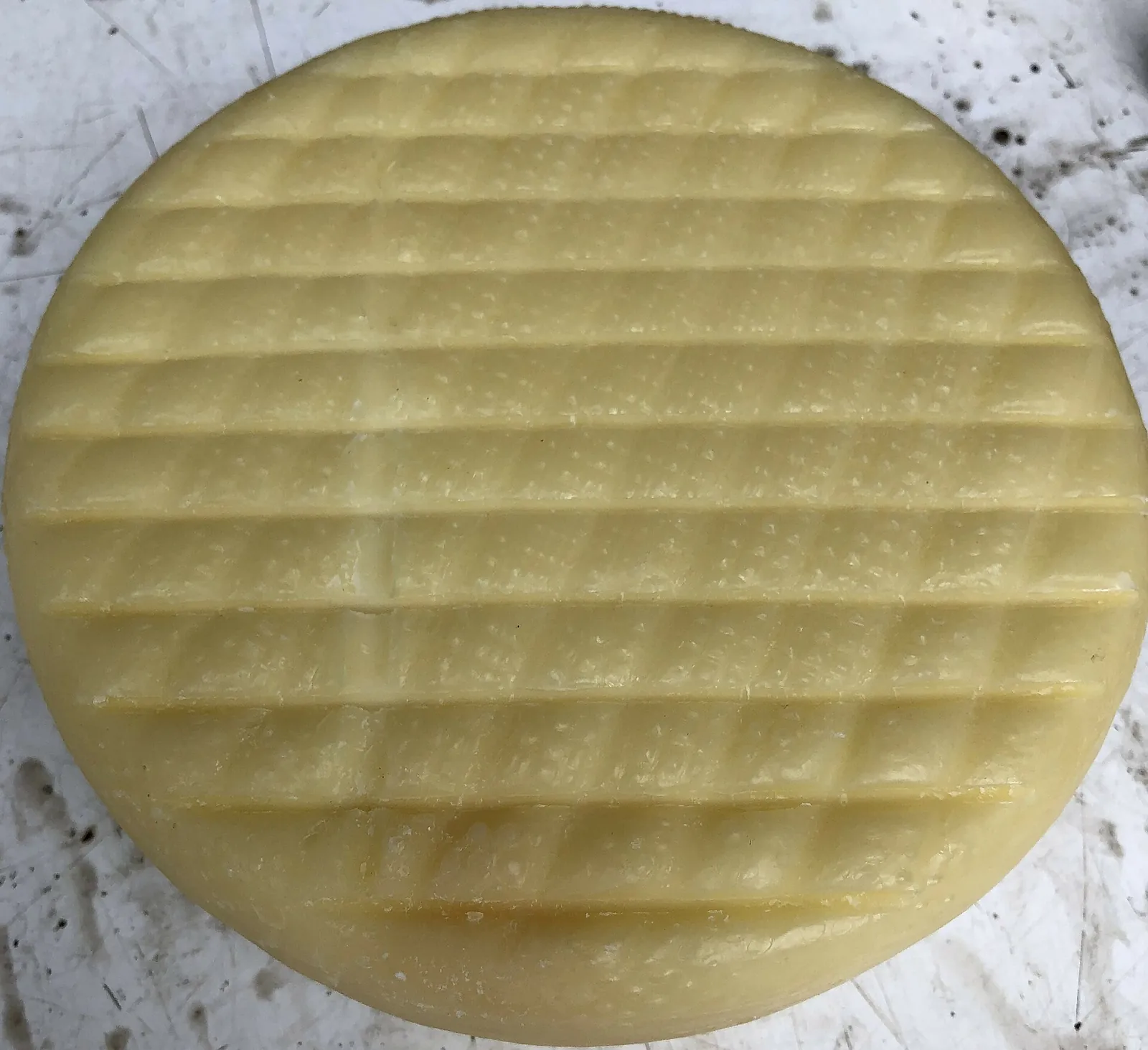 The top of a pale yellow Caciotta wheel showing the grid pattern pressed into the rind by its basket mold