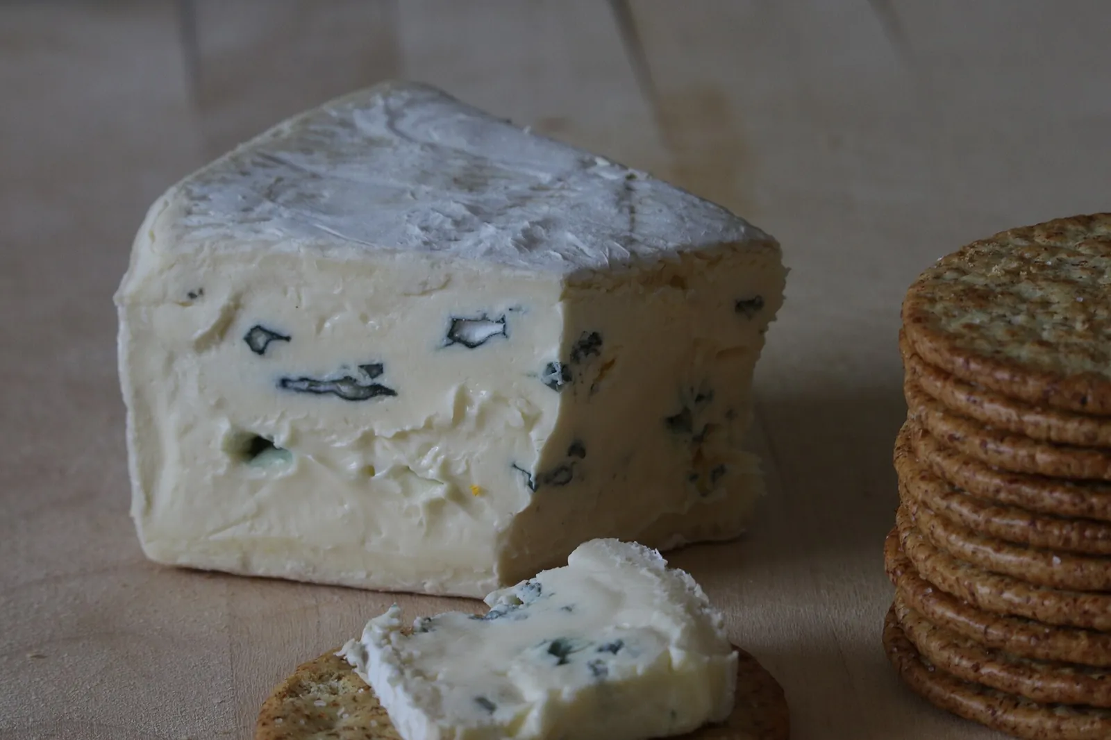 A wedge of Cambozola with a white bloomy rind and blue veins, next to crackers