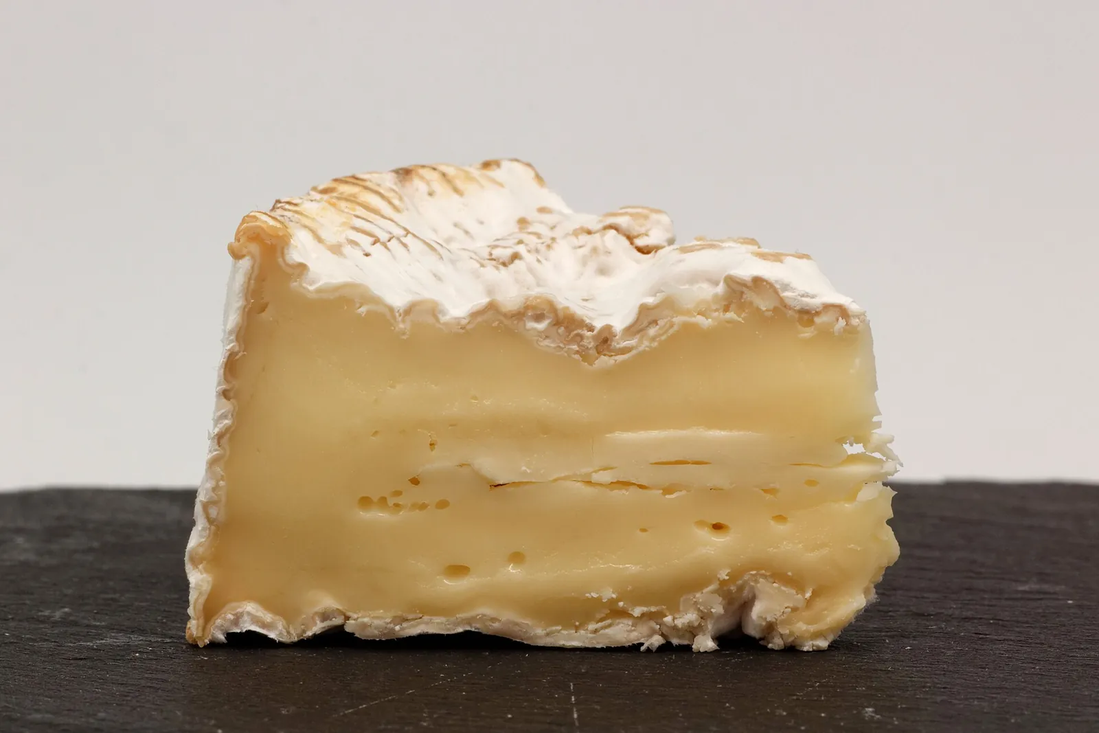 A wedge of Camembert de Normandie with a white bloomy rind and a soft, glossy center