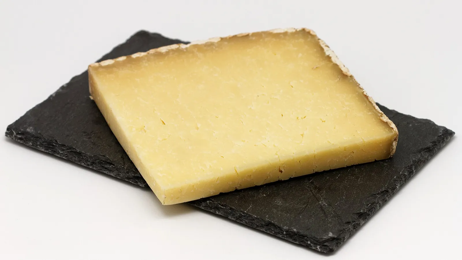 A thick slice of Cantal with pale golden paste and a natural rind edge resting on a slate board