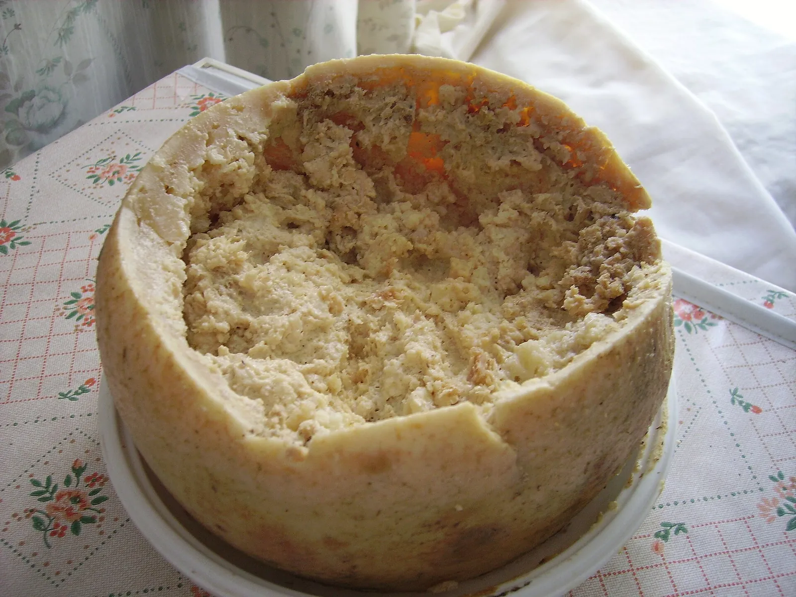 A whole Casu Marzu pecorino with its top cut away showing the soft creamy interior, on a plate