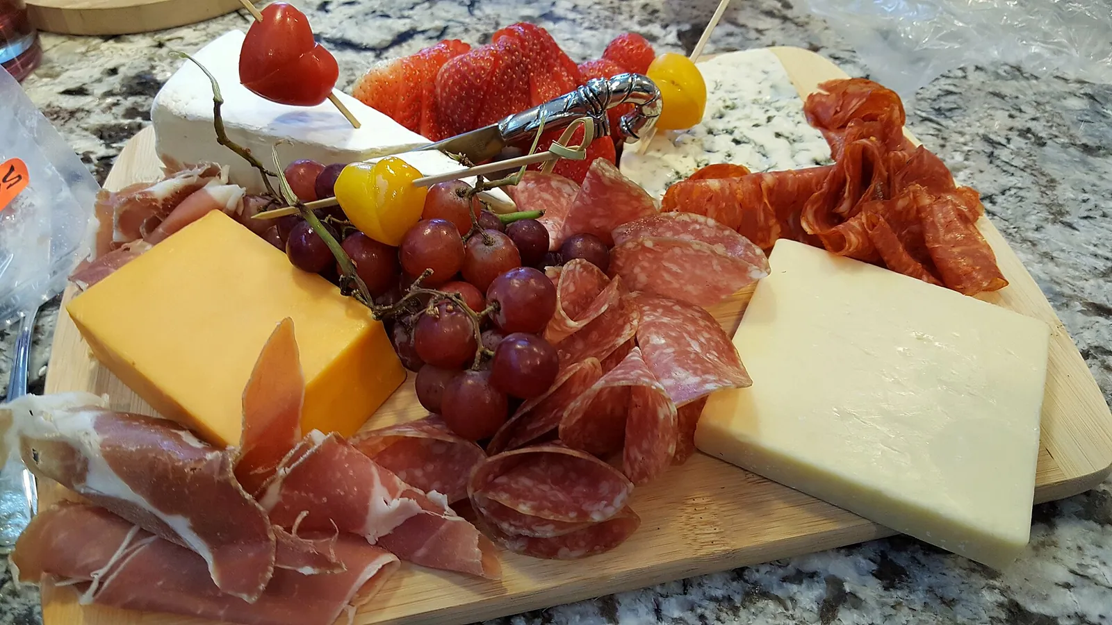 A board of cheddar and other cheeses with prosciutto, grapes and strawberries