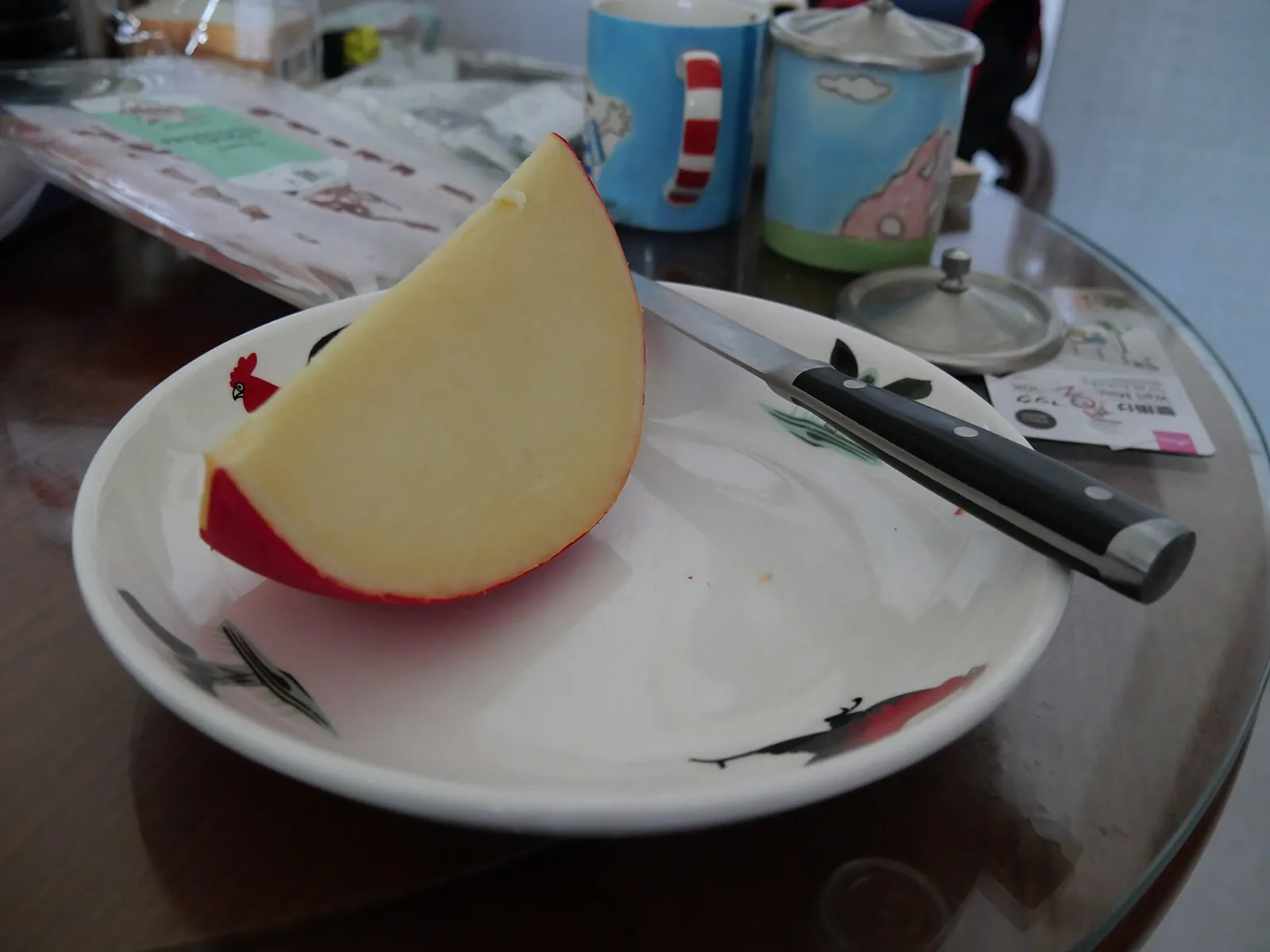 A wedge of Edam cheese with its red rind on a white plate beside a small knife.