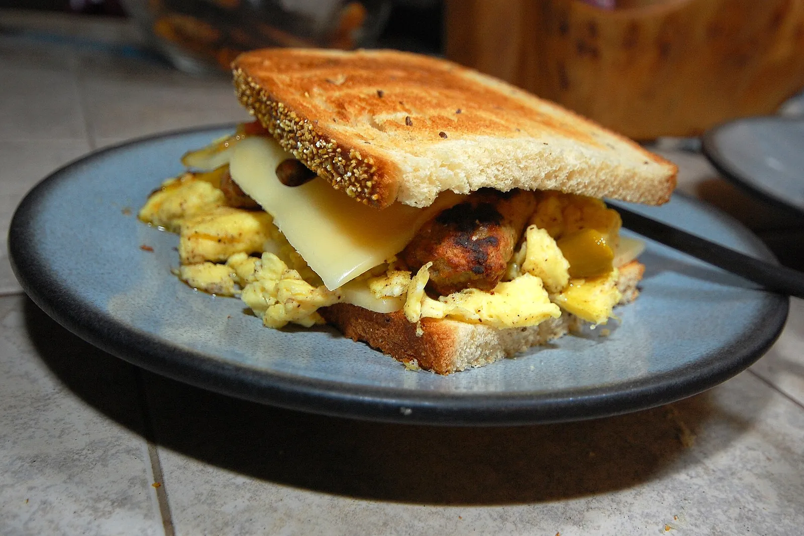 A toasted breakfast sandwich filled with scrambled egg and melted cheese, served on a blue plate.