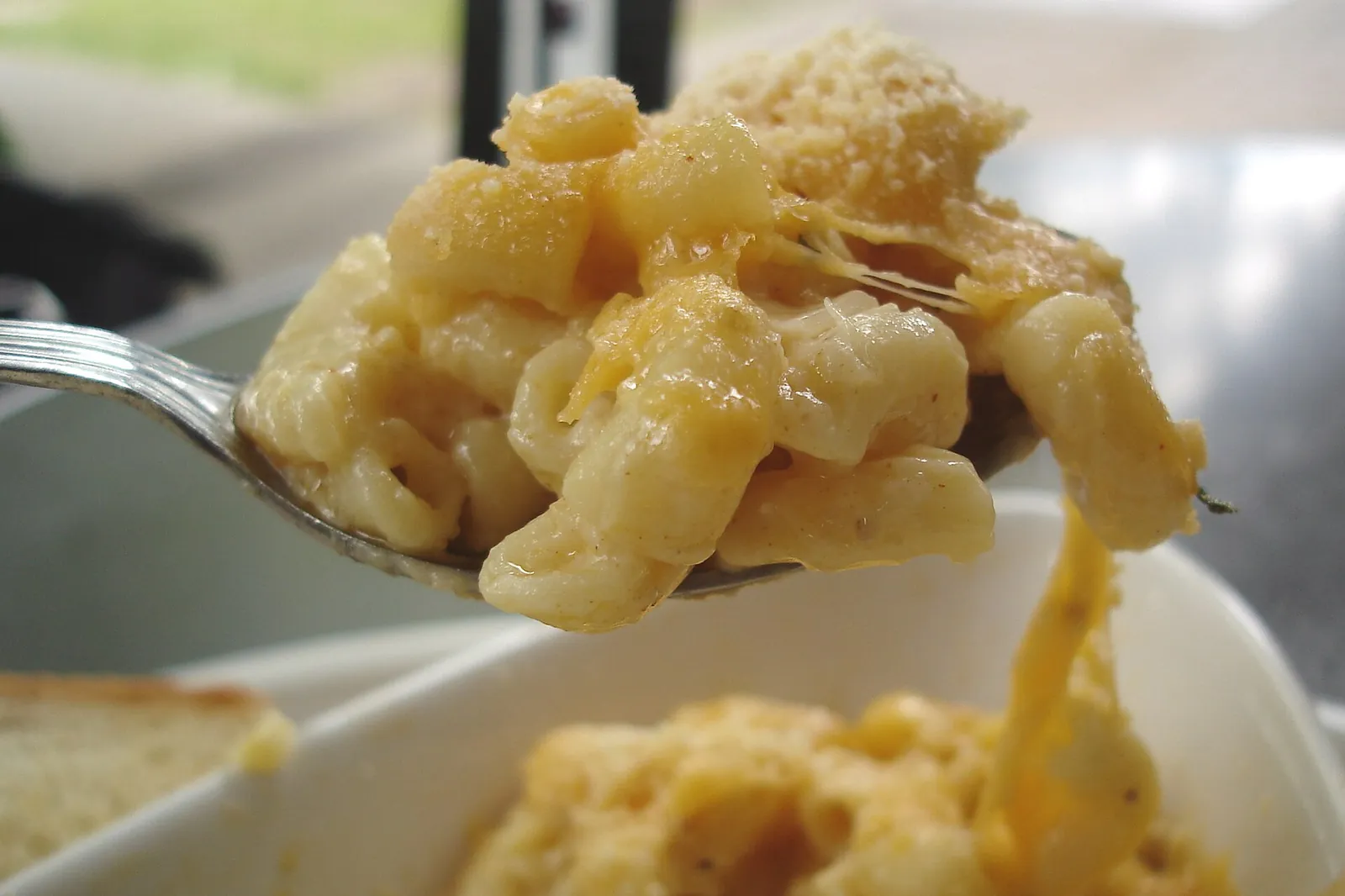 A forkful of baked macaroni and cheese lifted on a spoon, the creamy golden cheese sauce stretching back to the bowl.