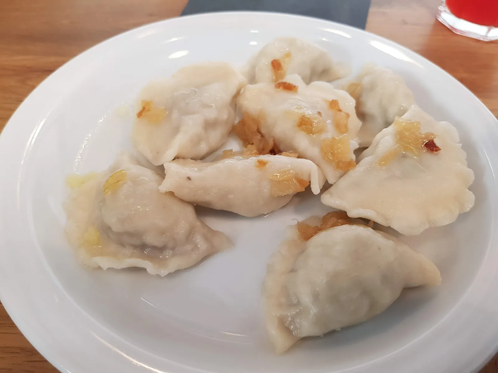 A plate of boiled pierogi ruskie, half-moon dumplings stuffed with potato and cheese, with browned onion