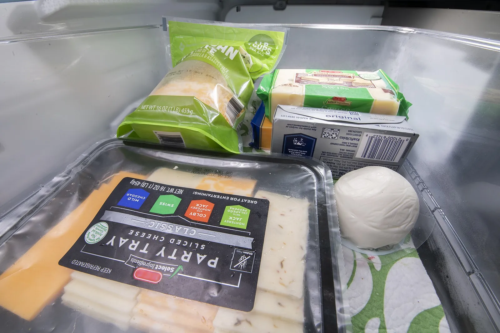 Packaged cheeses and a ball of mozzarella stored in a refrigerator drawer