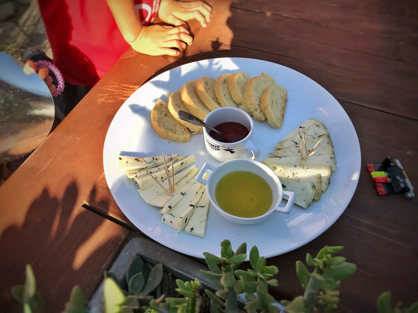 A white plate with slices of local cheese, fresh basil, tomato jam and a dish of olive oil on a wooden table.