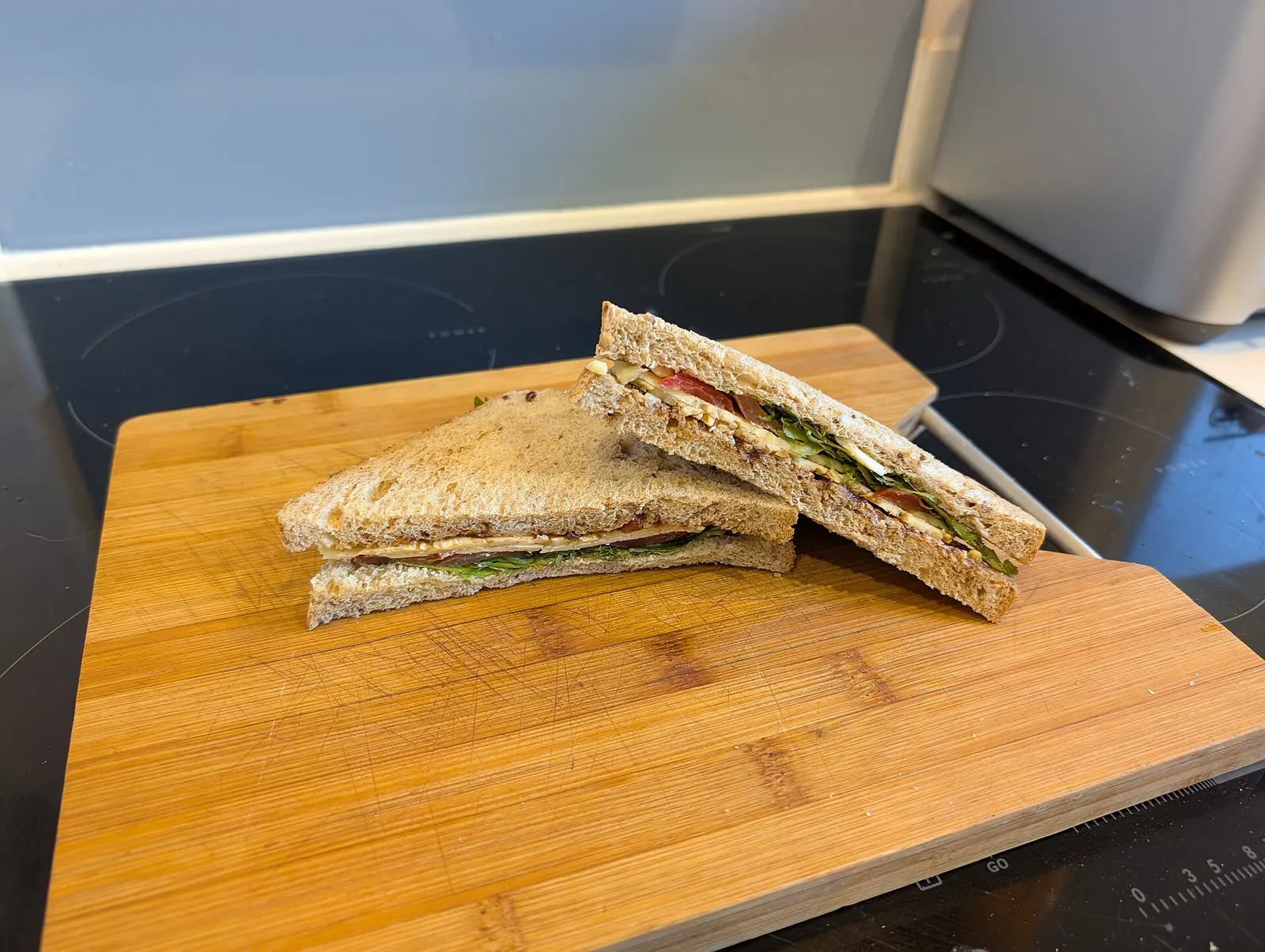 A cheese ploughman's sandwich cut into triangles on a wooden cutting board, with cheese and salad between the bread slices.