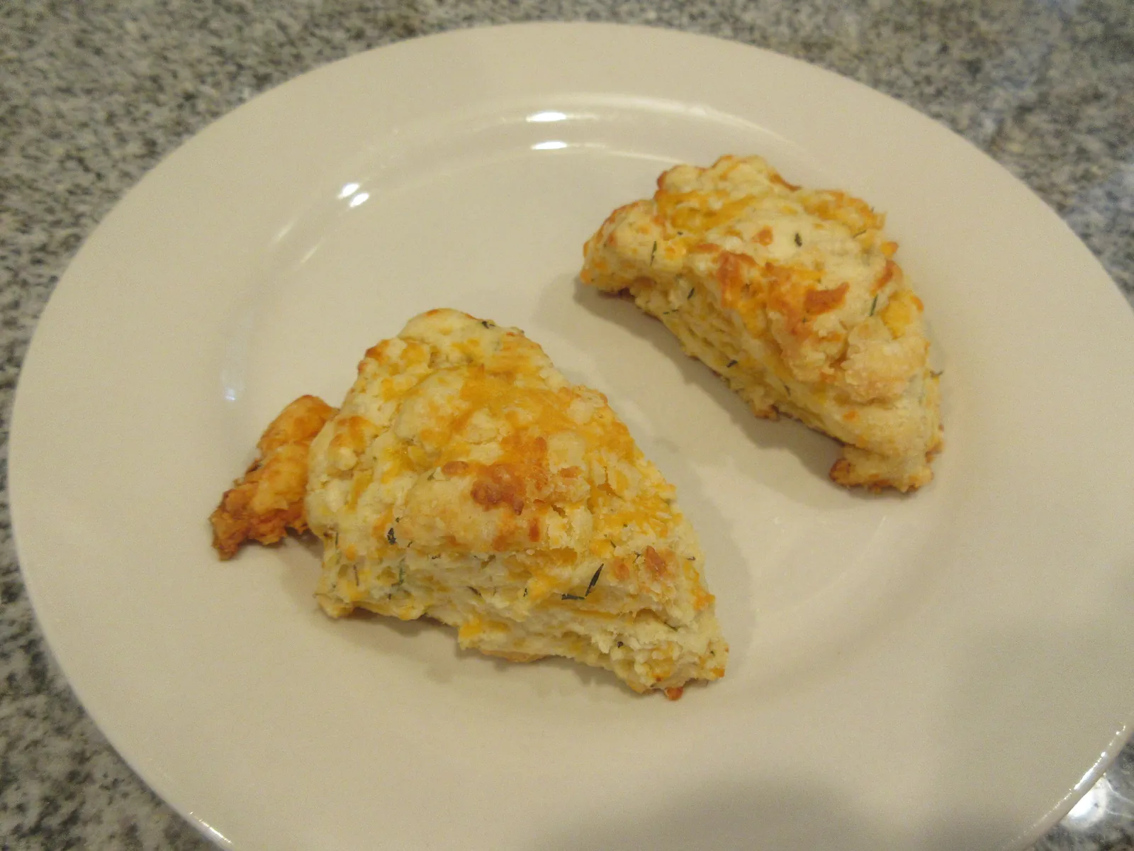 Two golden cheddar scones with a crisp browned top, one broken open, on a white plate