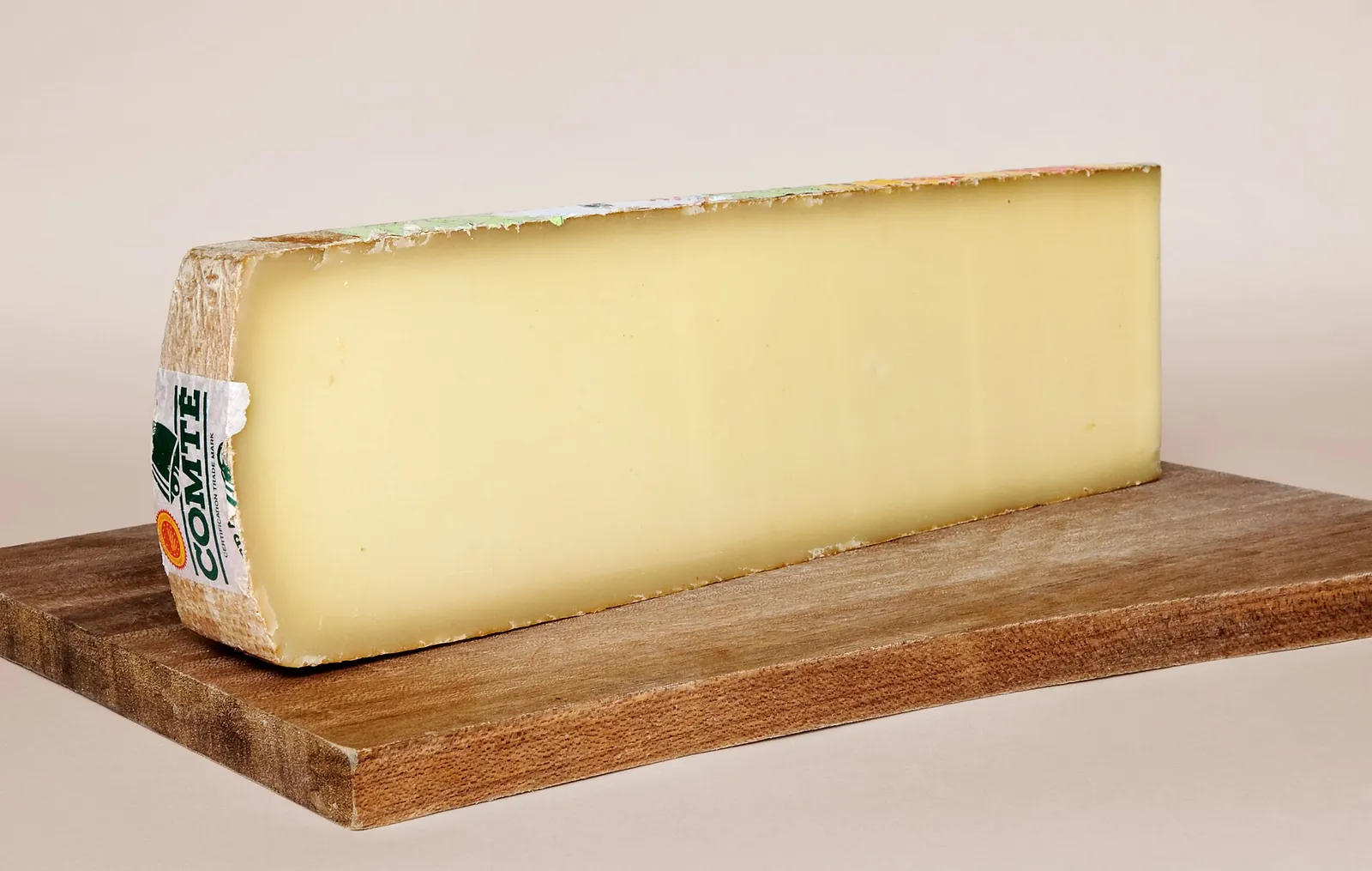 A long wedge of Comté with its brown rind on a wooden board
