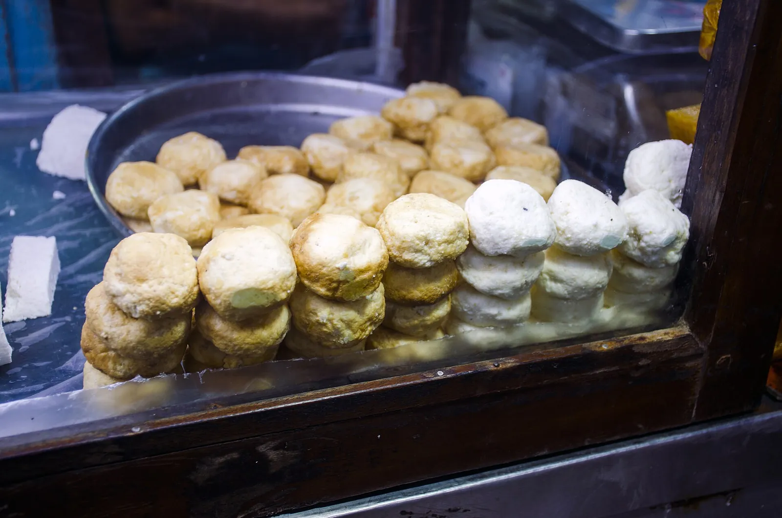 Stacked rounds of Bandel cheese, some plain and some smoked, piled in a glass case at a shop in Kolkata's New Market, India.