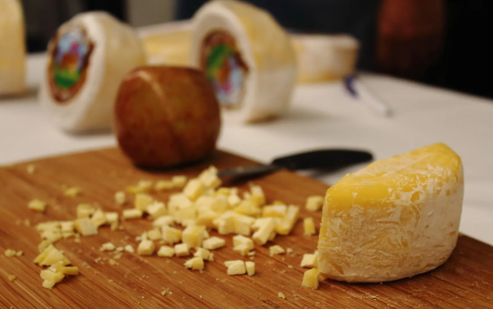 Several cheeses made in Querétaro, Mexico, on a wooden board, including a yellow wedge with diced cheese beside it and rounds in colorful labels.