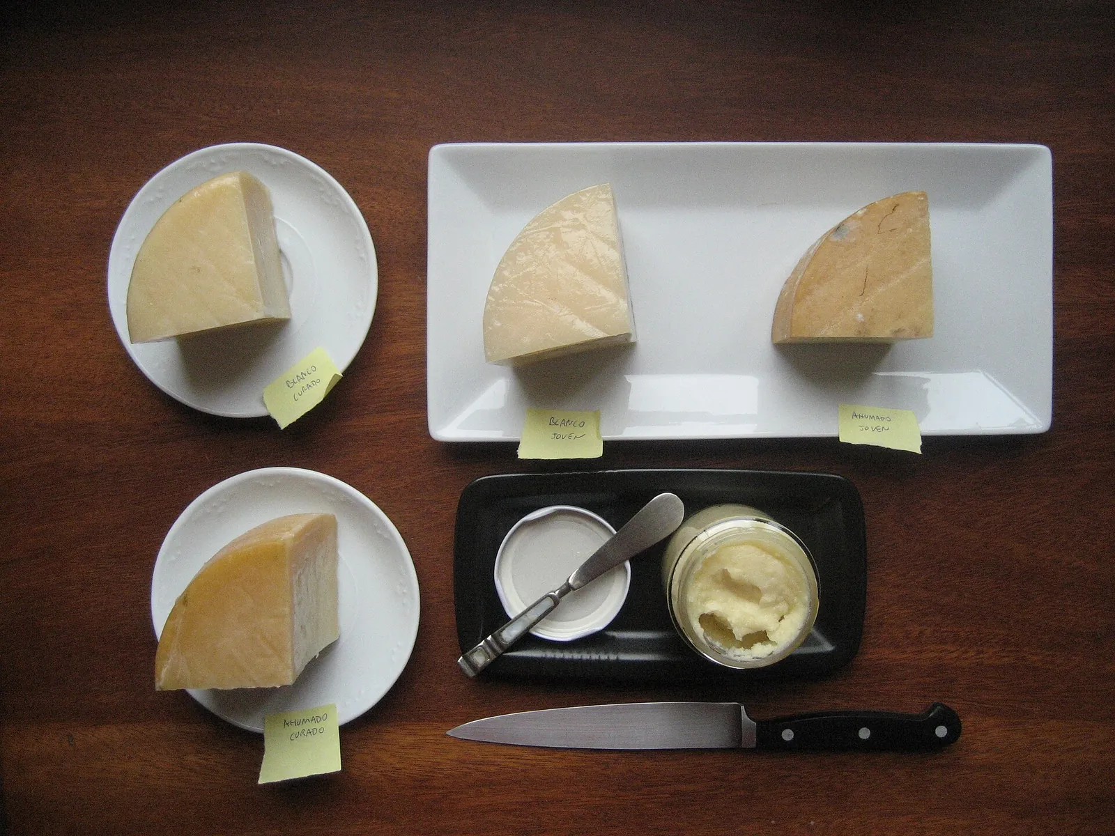 Wedges of Basque cured and smoked Idiazabal sheep cheese on white plates beside a small dish and a knife, seen from above.