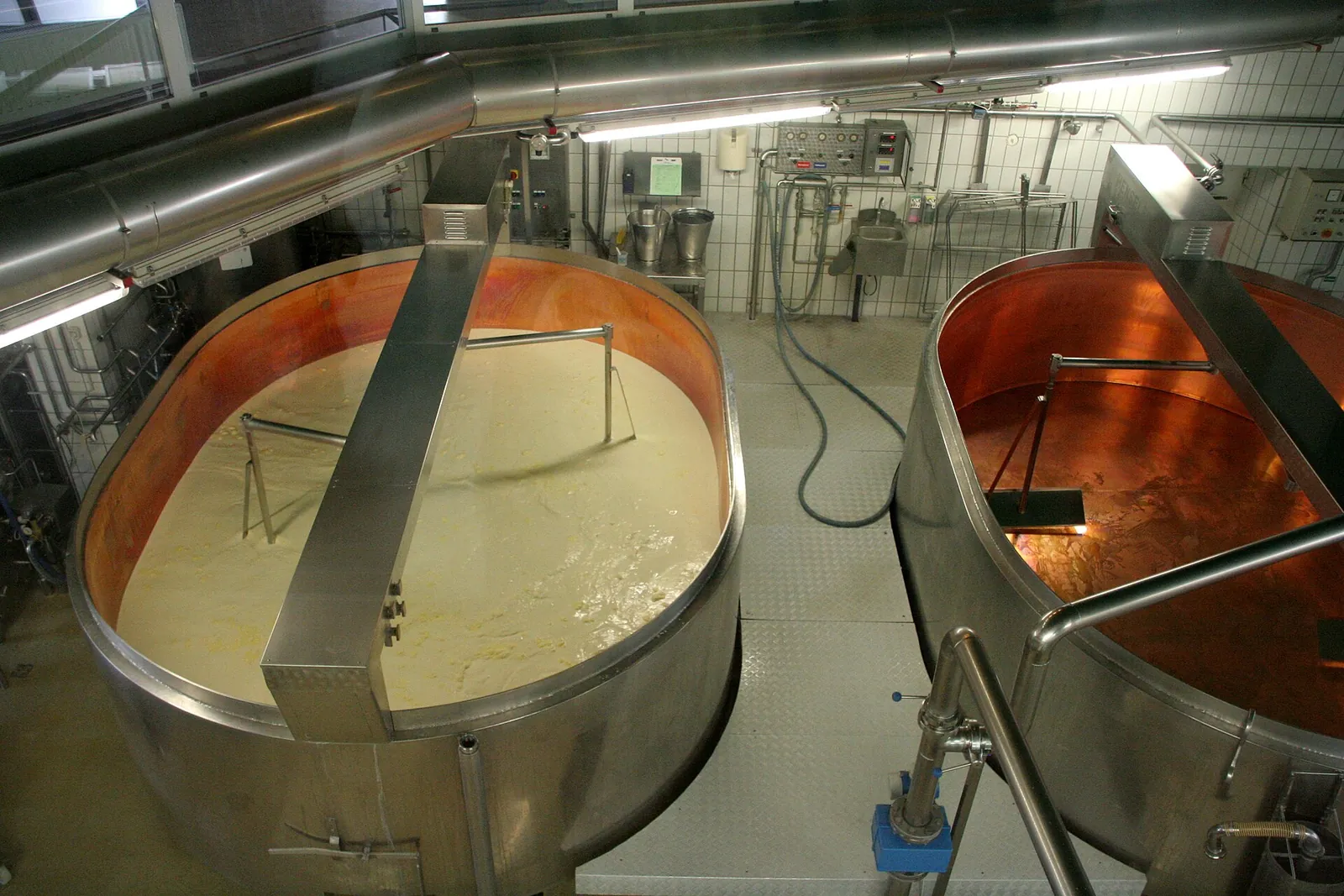 Overhead view of two large vats of milk and curd, one lined with copper, in a Swiss dairy making Emmentaler cheese.