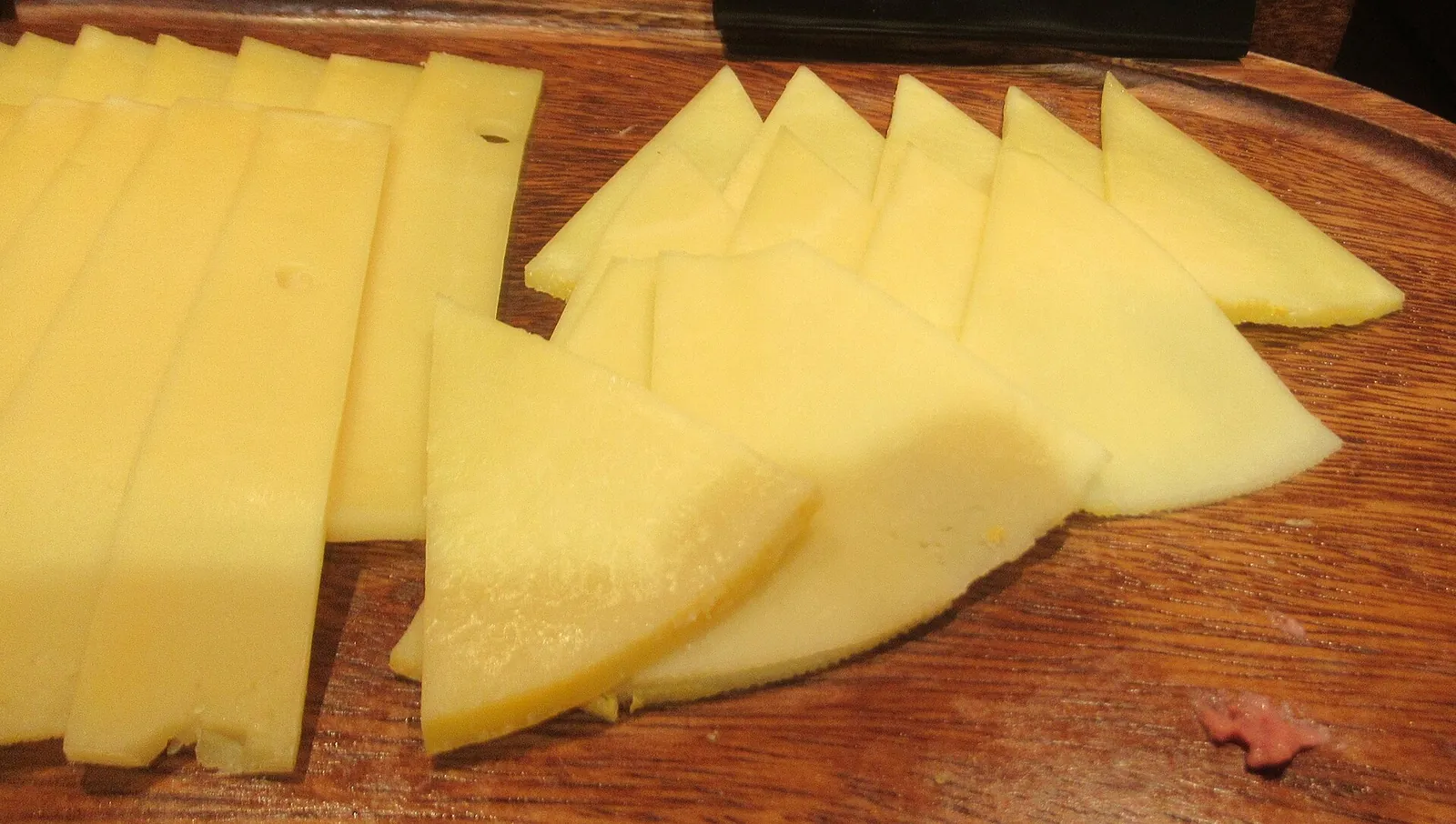 Thin slices of yellow Gouda-style cheese cut into long strips and triangles on a wooden board.