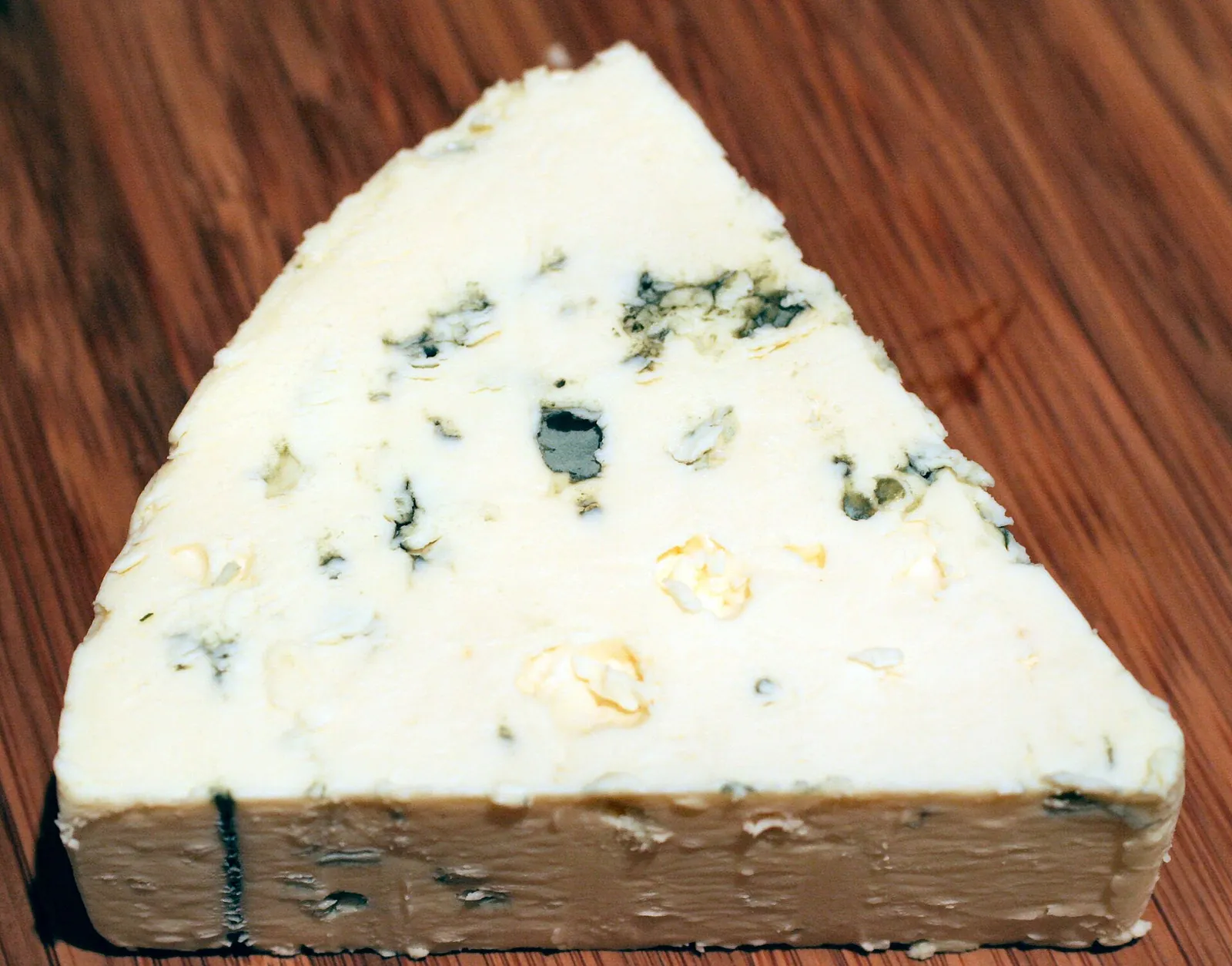 A wedge of Danish Blue with scattered blue veins on a wooden board