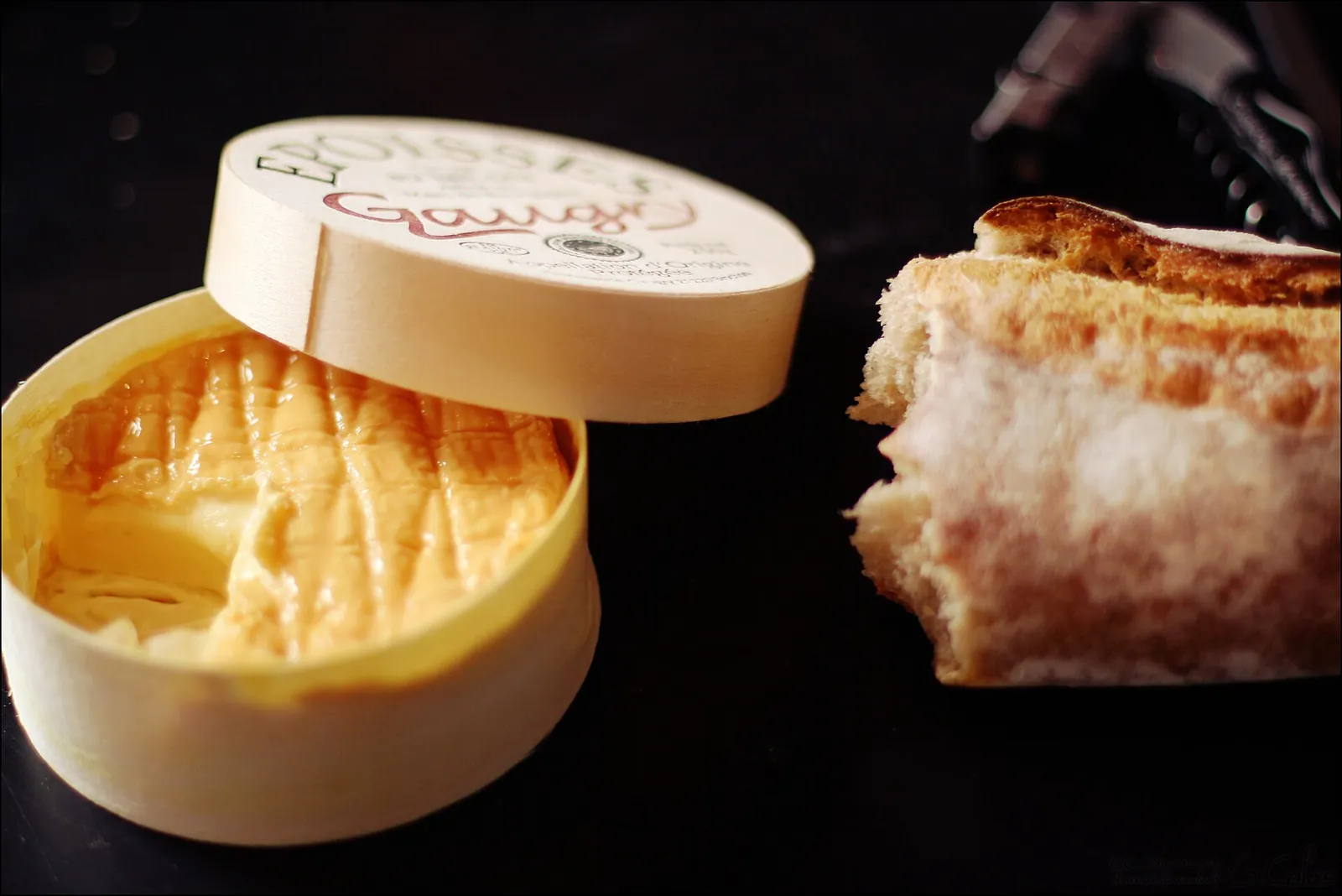 A round of Époisses with its orange washed rind in a wooden box, next to bread spread with the runny cheese