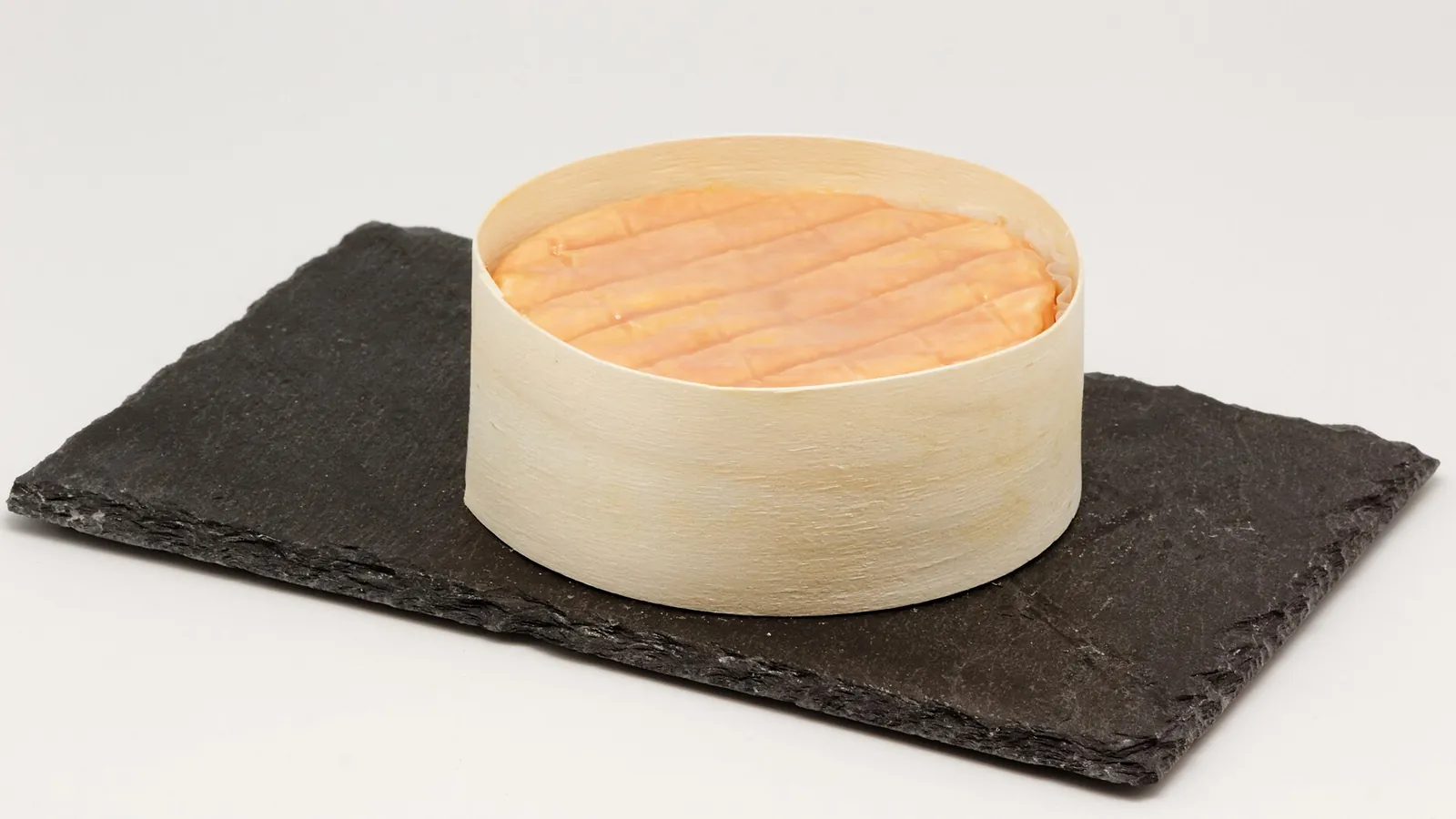 A round of Époisses in its wooden box, its orange washed rind showing at the top, on slate