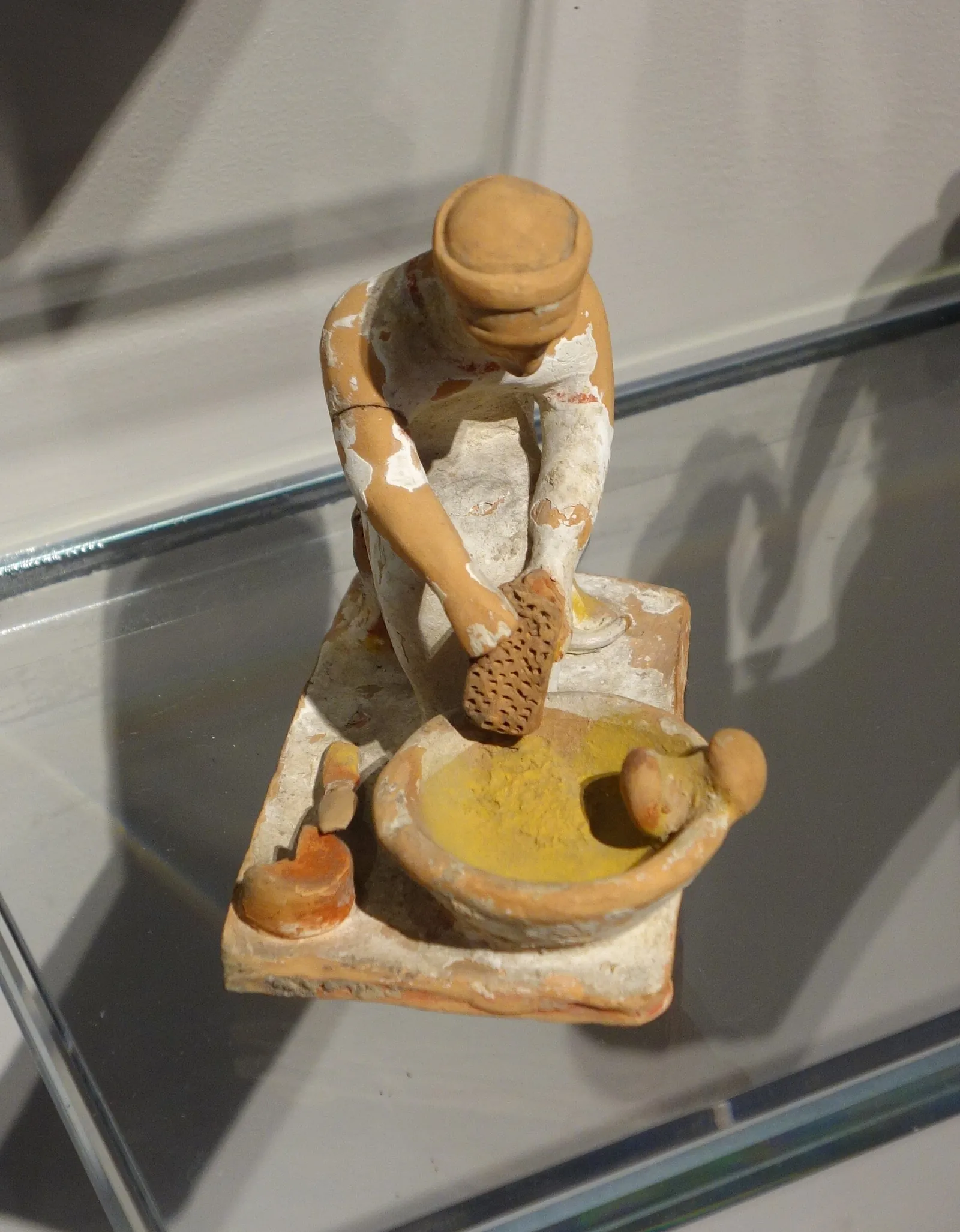 An ancient Greek terracotta figurine of a woman grating cheese into a bowl
