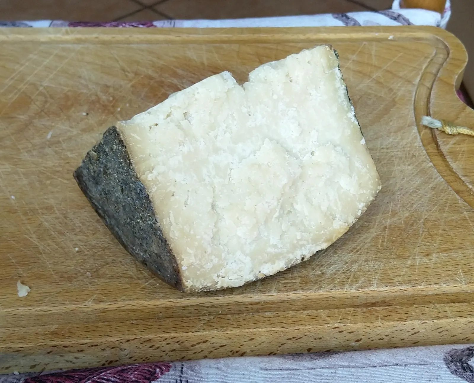 A wedge of Fiore Sardo with a dark rind and pale firm paste on a wooden cutting board