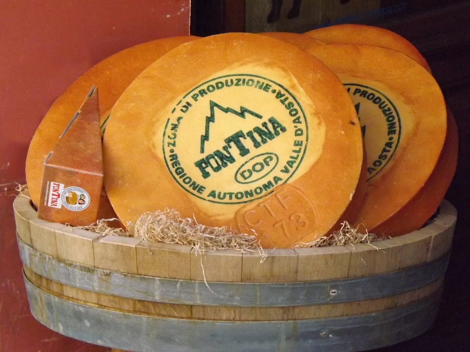 Wheels of Fontina in a wooden tub, the top one stamped with the Fontina DOP mark