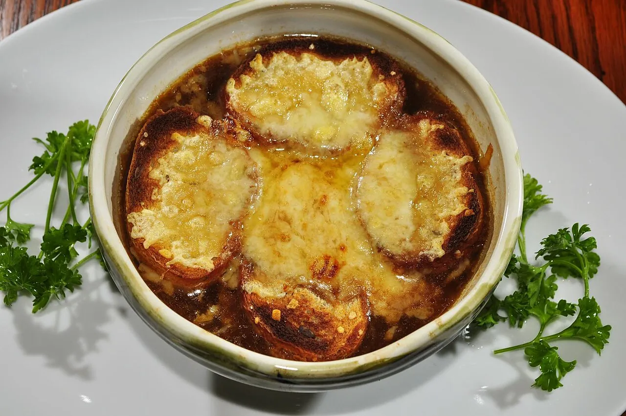 A crock of French onion soup under a bubbling, browned layer of melted cheese on toasted bread, garnished with parsley