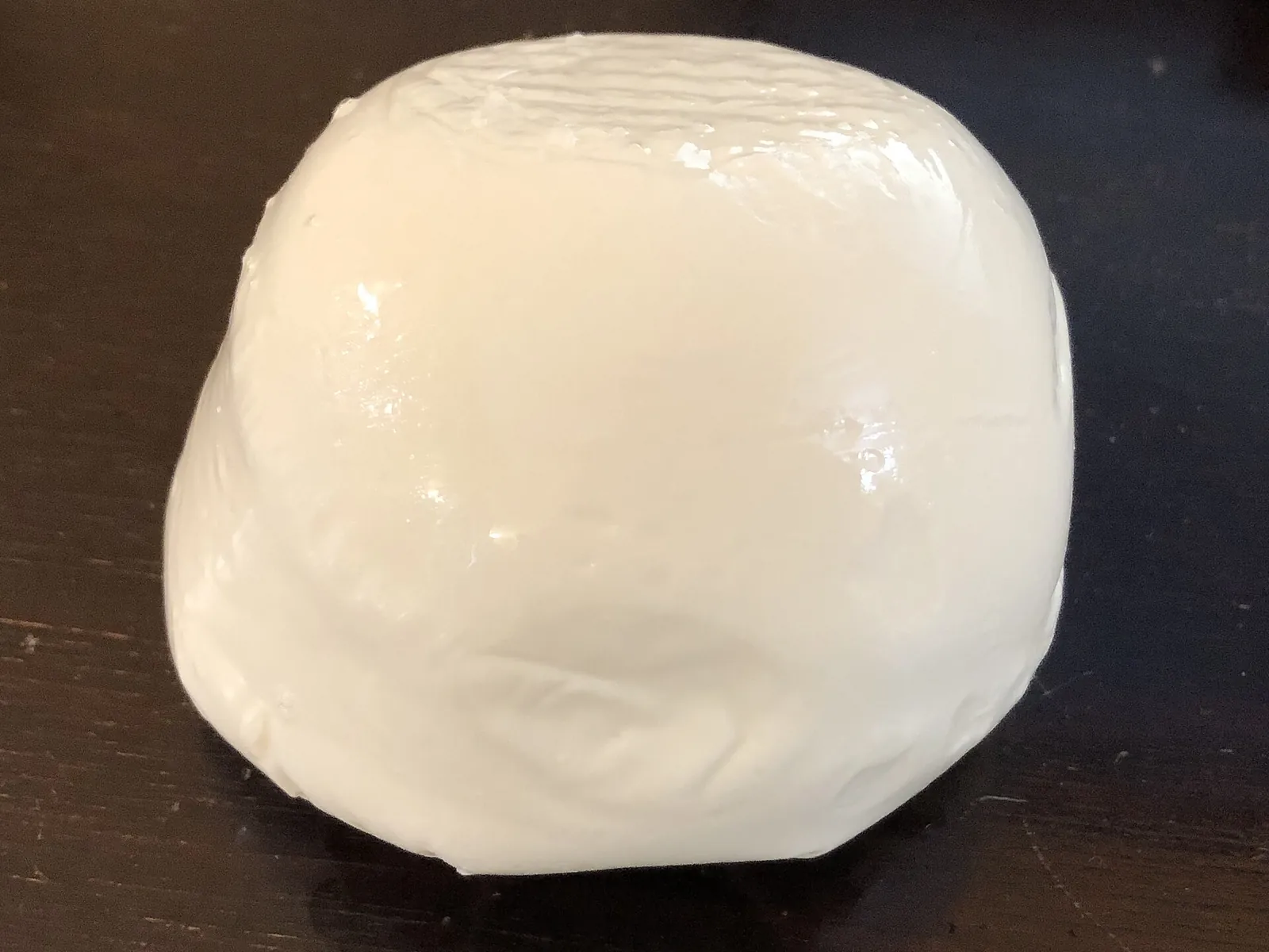 A ball of fresh white mozzarella on a dark background