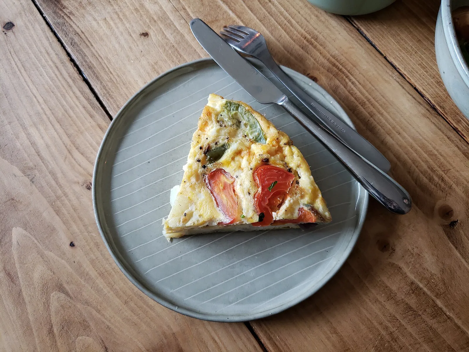 A wedge of cheese frittata with tomato on a gray plate with a knife and fork