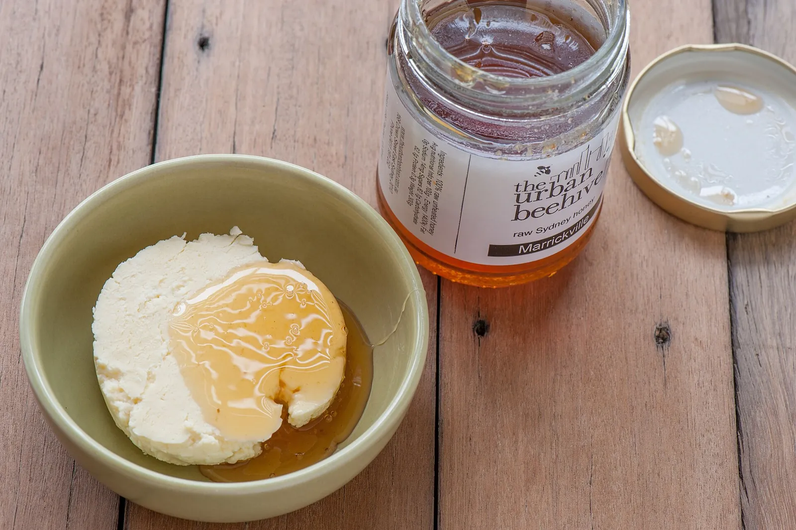 Fresh goat cheese in a bowl drizzled with honey, next to a jar of honey