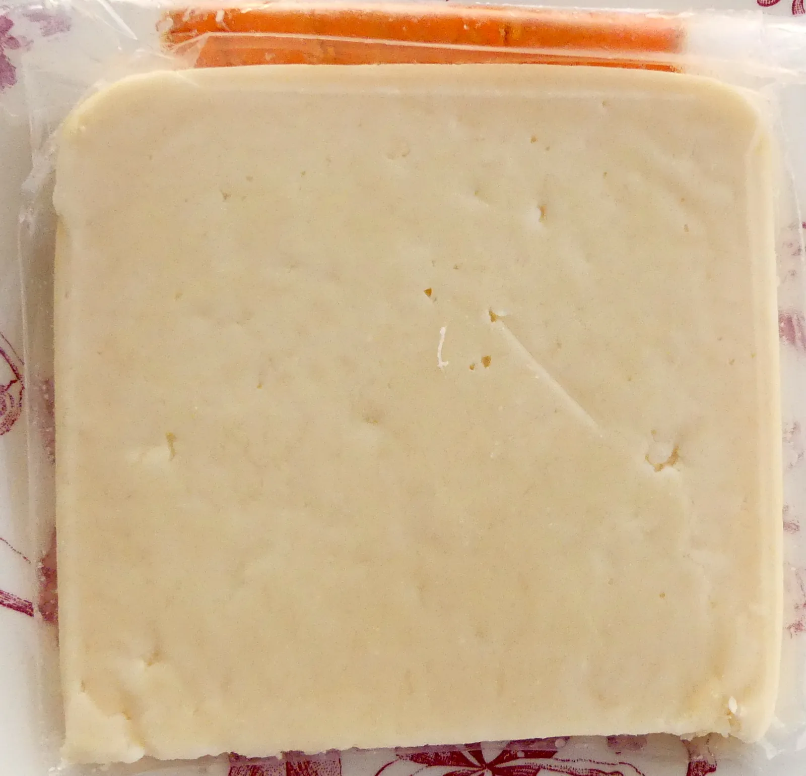 A flat square slice of pale yellow Graviera cheese lying on its packaging
