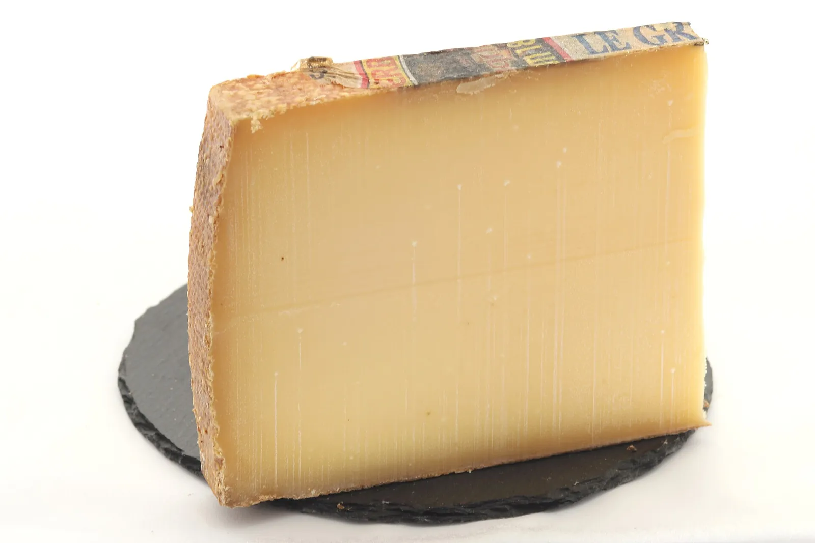 A tall wedge of Gruyère with its brown rind on a round slate