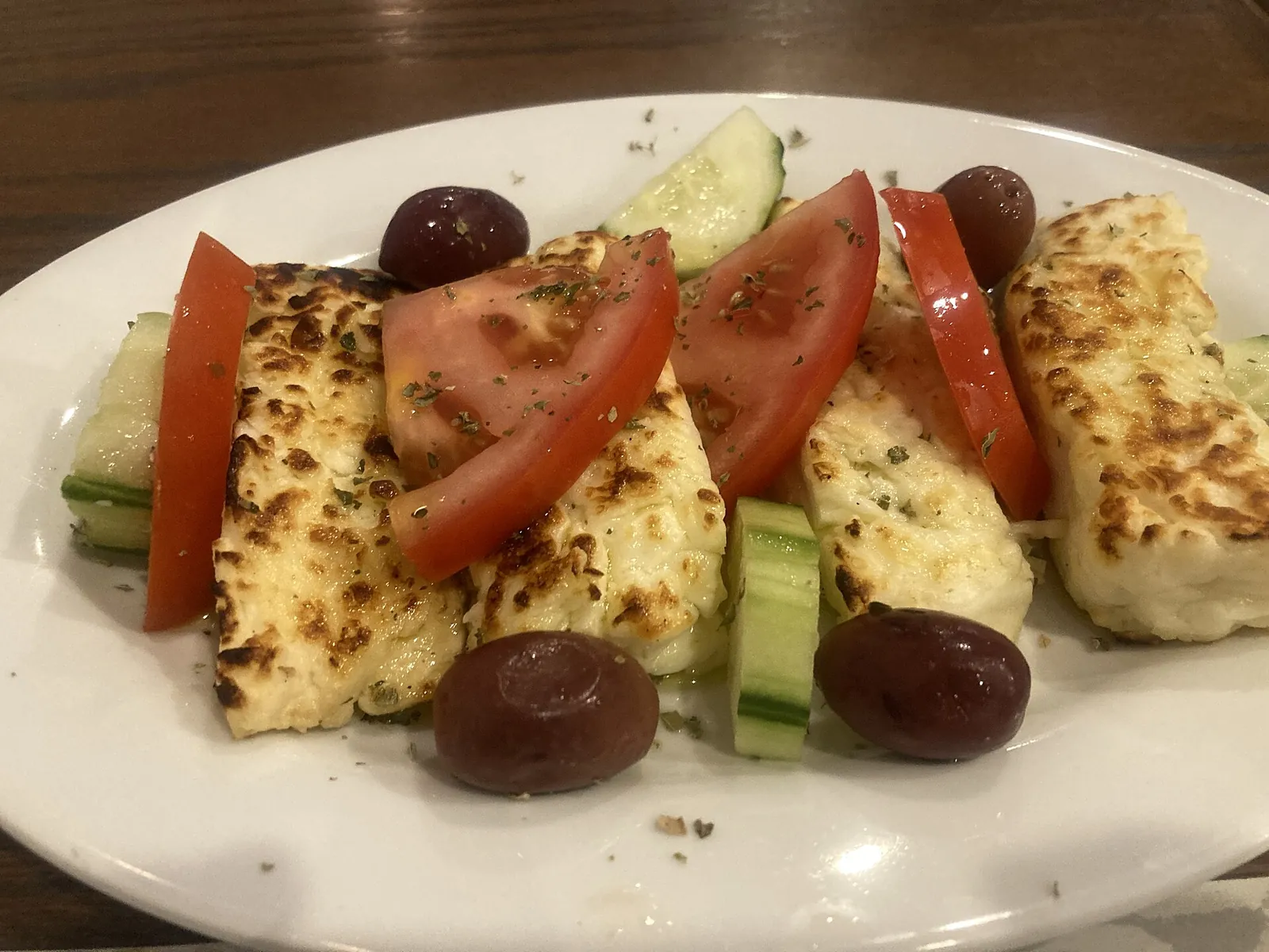 Grilled halloumi with tomato, cucumber and black olives on a white plate