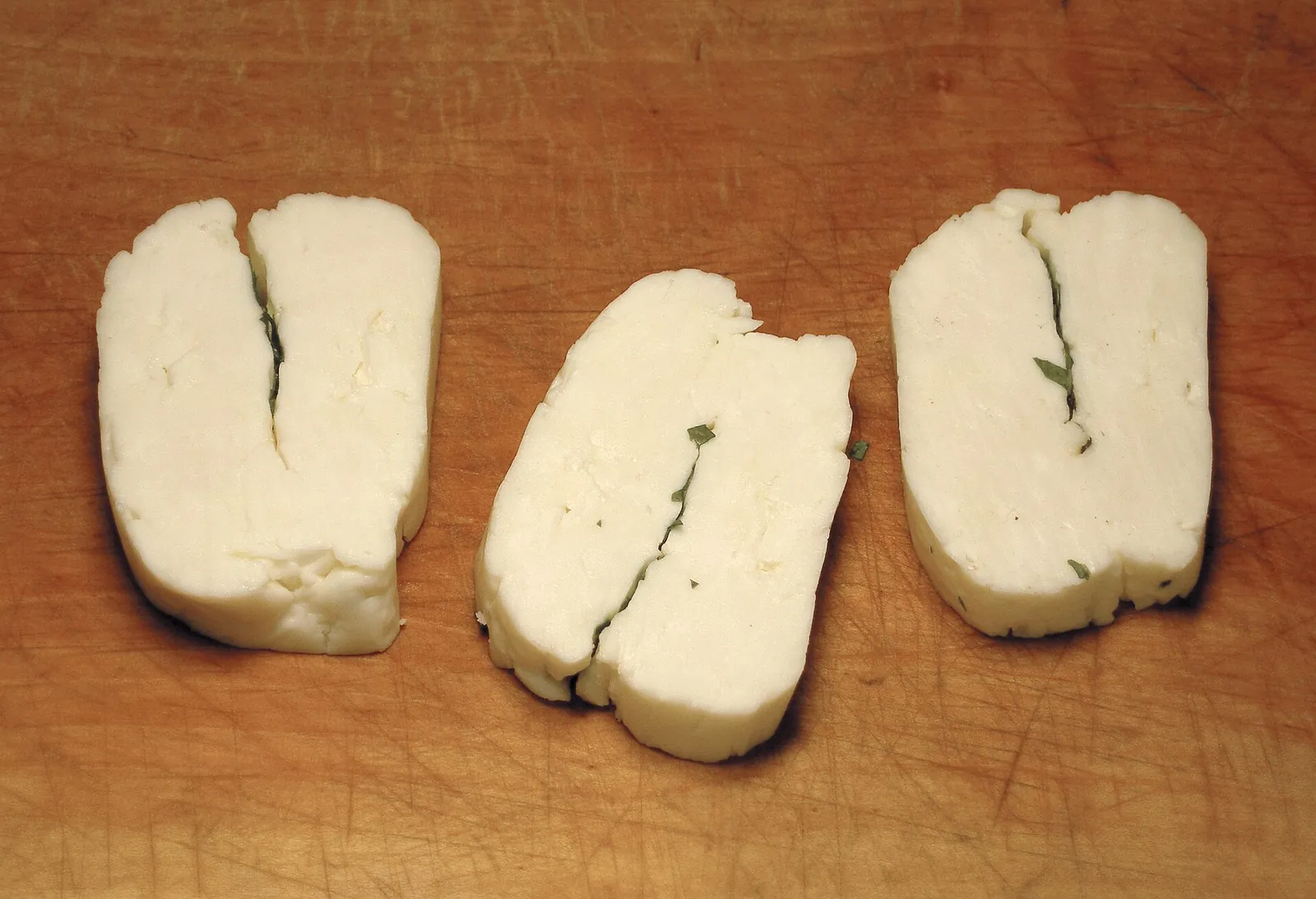 Slices of halloumi on a wooden board, each showing the split where the cheese was folded, with flecks of mint