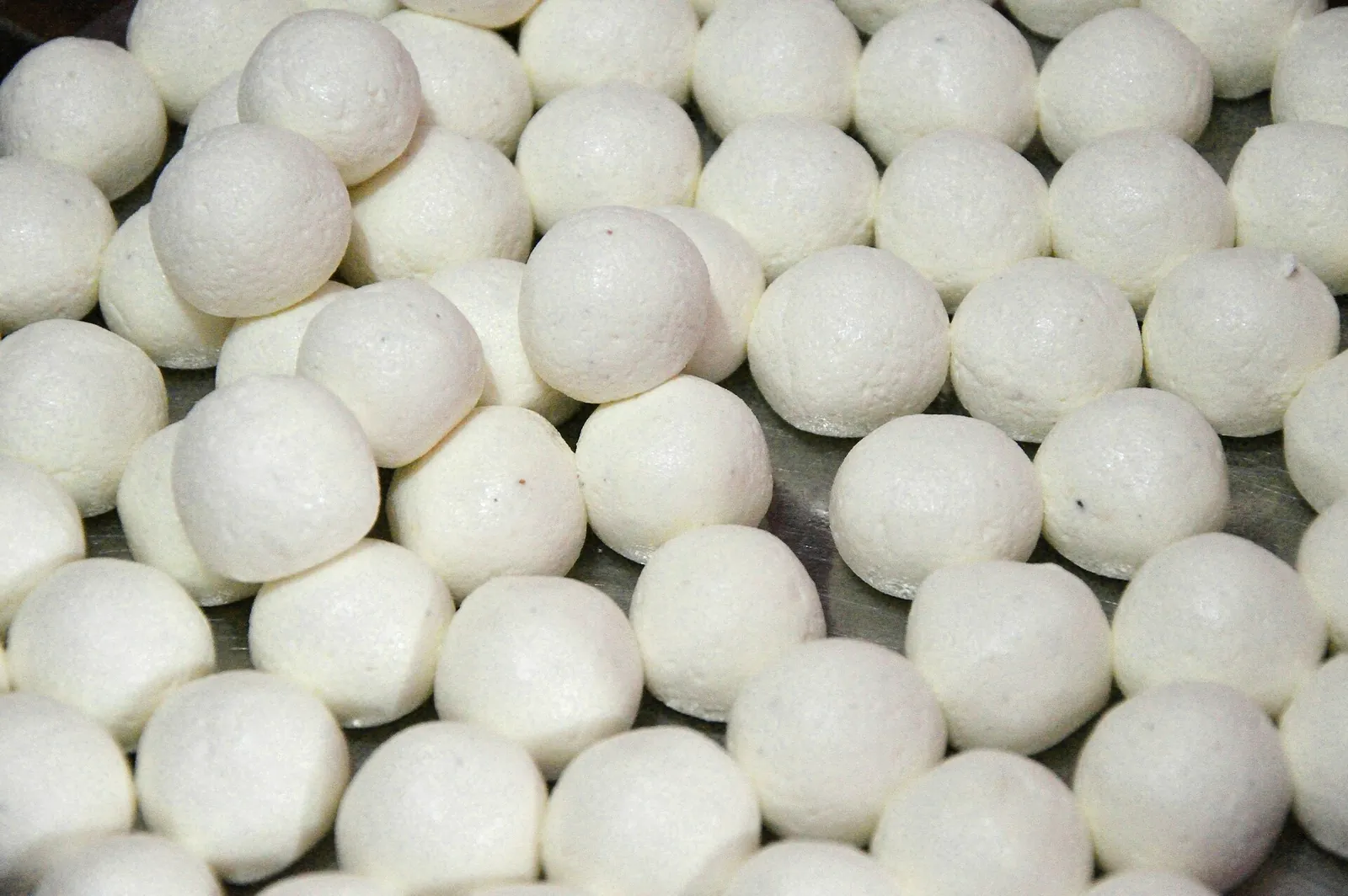 Dozens of round white chhena balls, a fresh Indian curd cheese, laid out on a steel tray before being cooked for rasgulla.