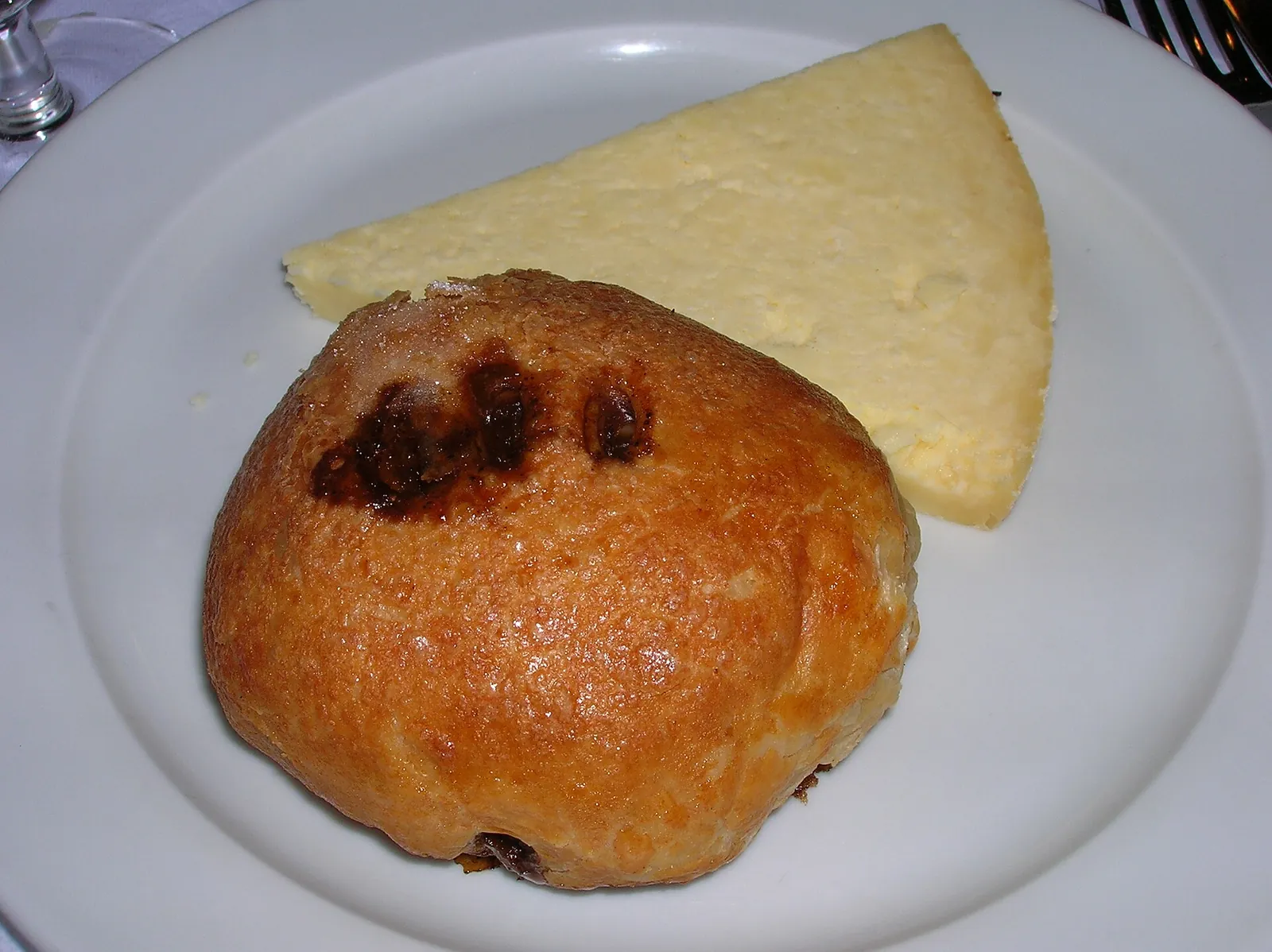 A wedge of pale crumbly Lancashire cheese beside an Eccles cake on a white plate