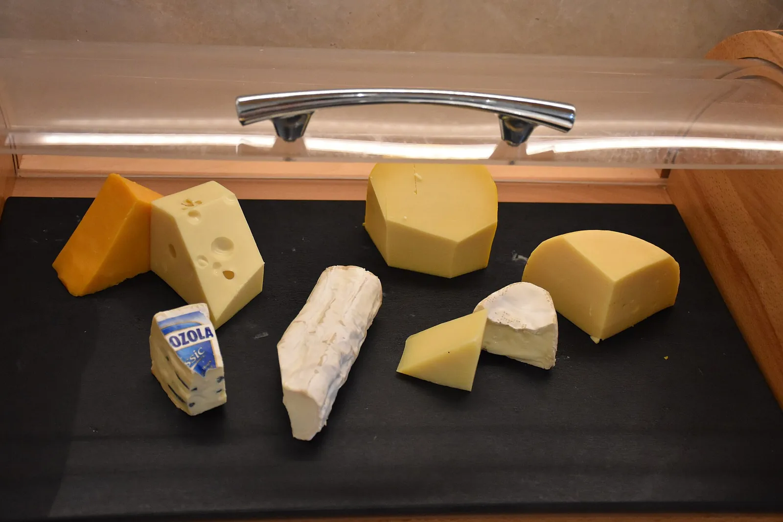 Assorted cheese pieces on a black counter: an orange wedge, a holey Swiss, a rind covered log, a small brie and a yellow block.