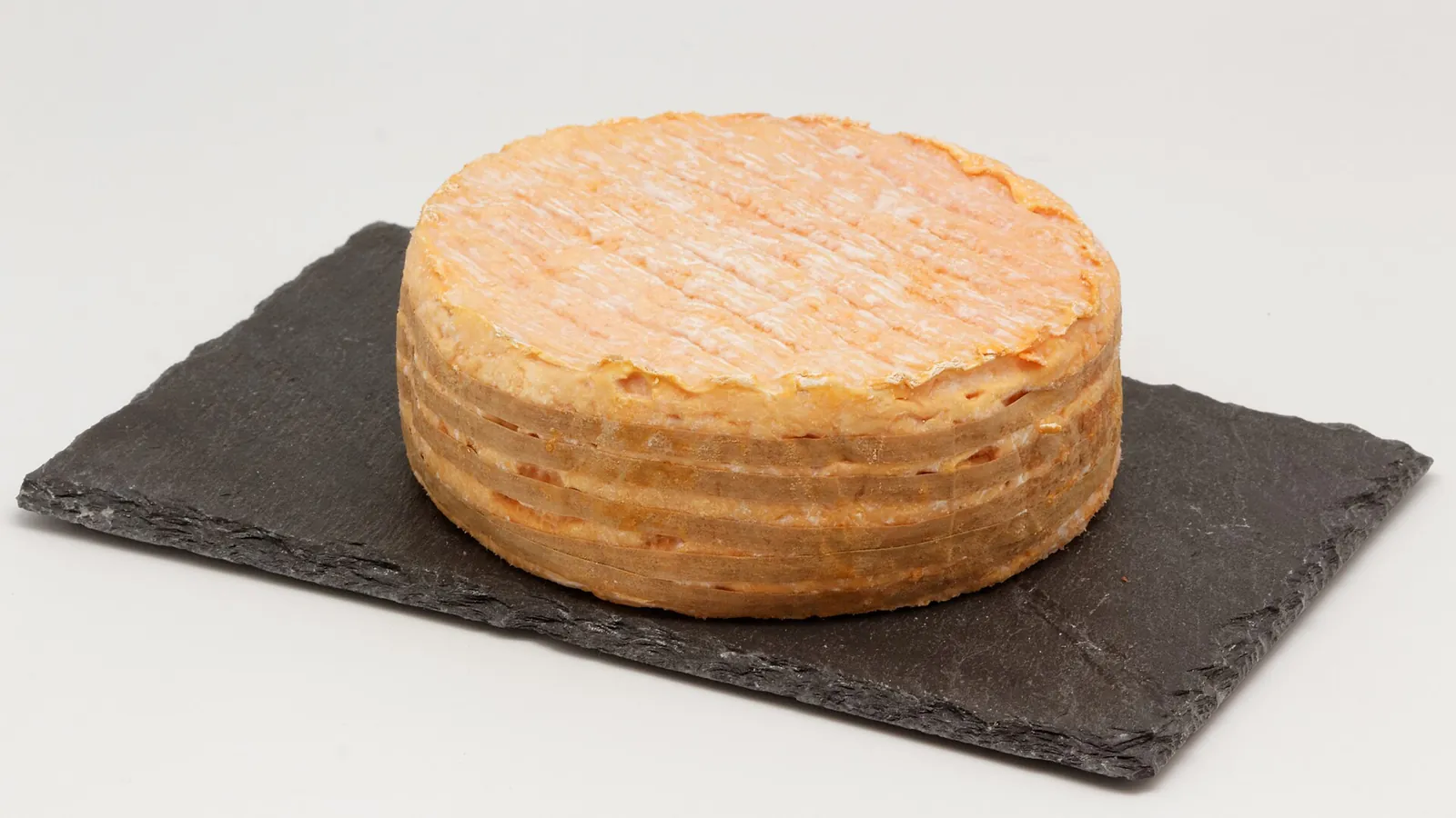 A round Livarot with an orange washed rind wrapped in several bands, on a slate board
