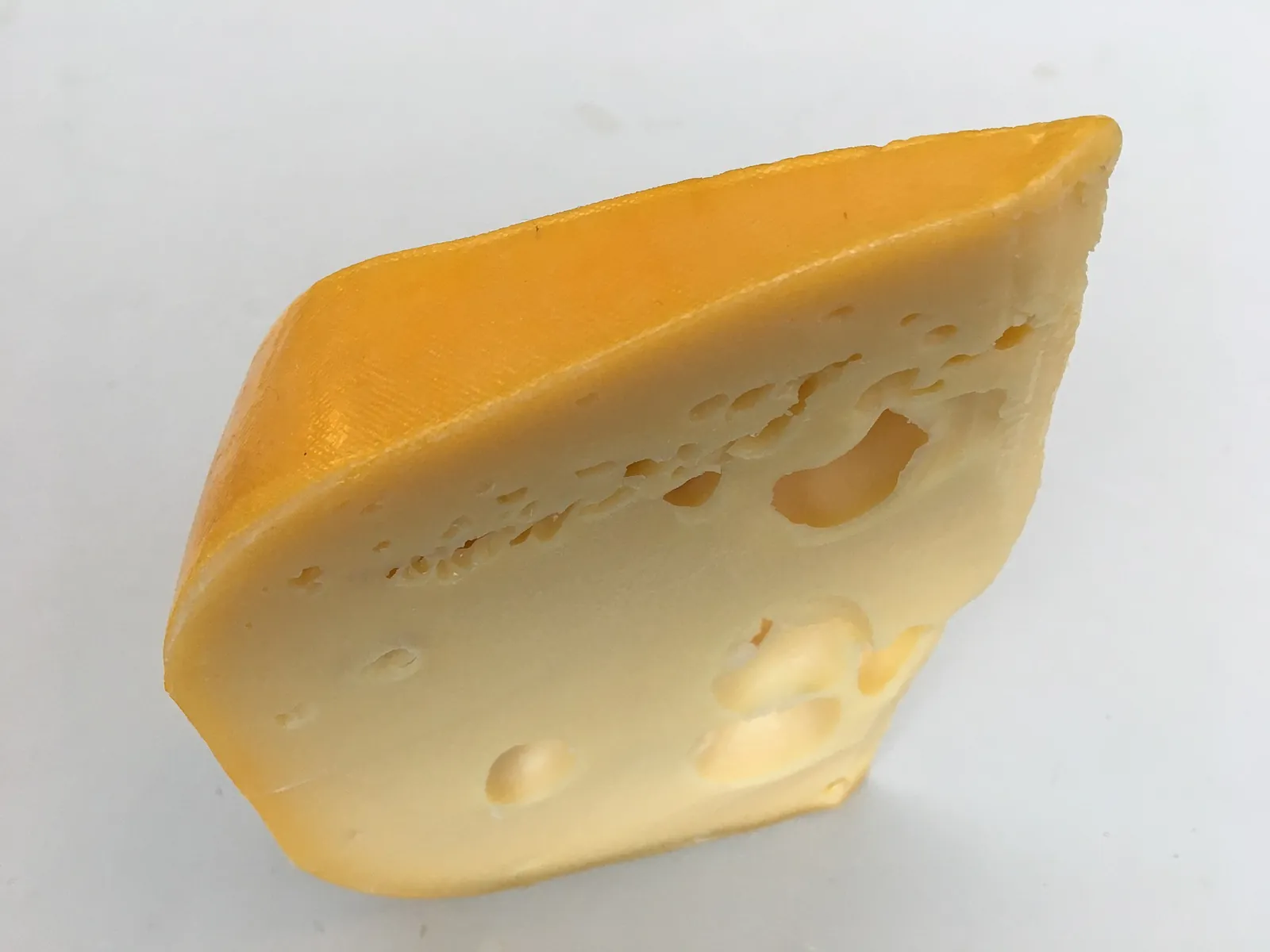 A wedge of Dutch Maasdam-style cheese with large holes and a yellow rind