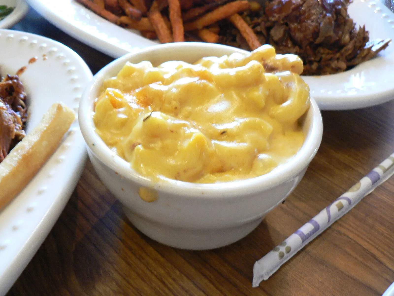 A white bowl of creamy macaroni and cheese on a restaurant table, the elbow pasta coated in a glossy orange cheese sauce.